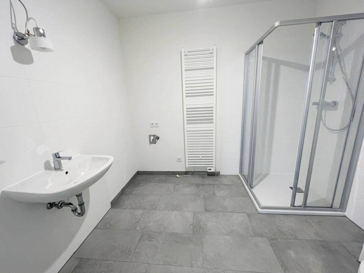 Modernes Badezimmer mit Duschkabine, Waschbecken und beheiztem Handtuchhalter in neutralen Farben.