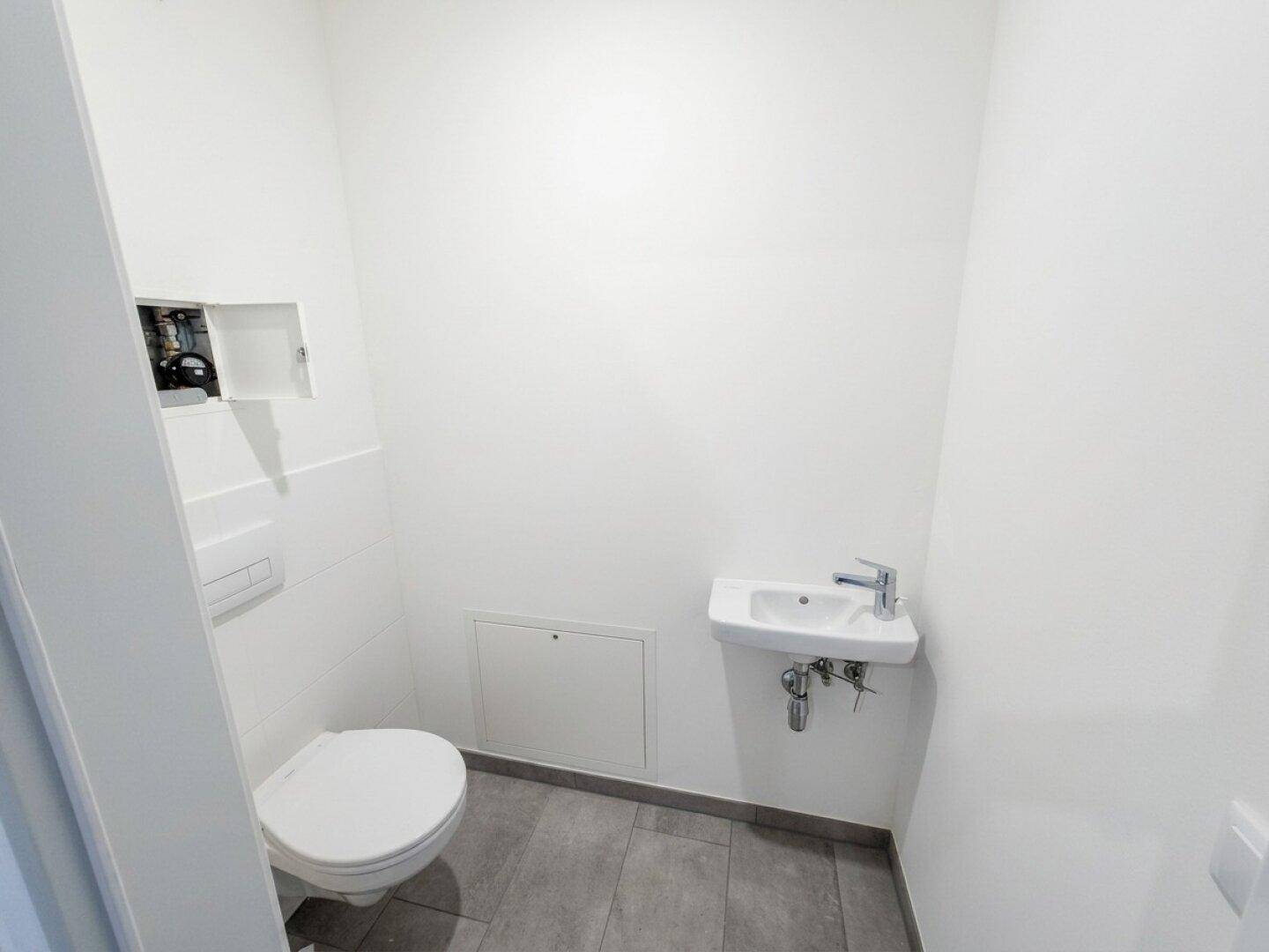 Modernes Gäste-WC mit Wand-WC, kleinem Waschbecken und grauen Fliesenboden.