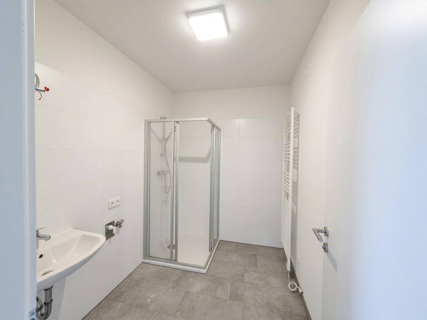 Helles Badezimmer mit Duschkabine, Waschbecken und beheiztem Handtuchhalter an der Wand.
