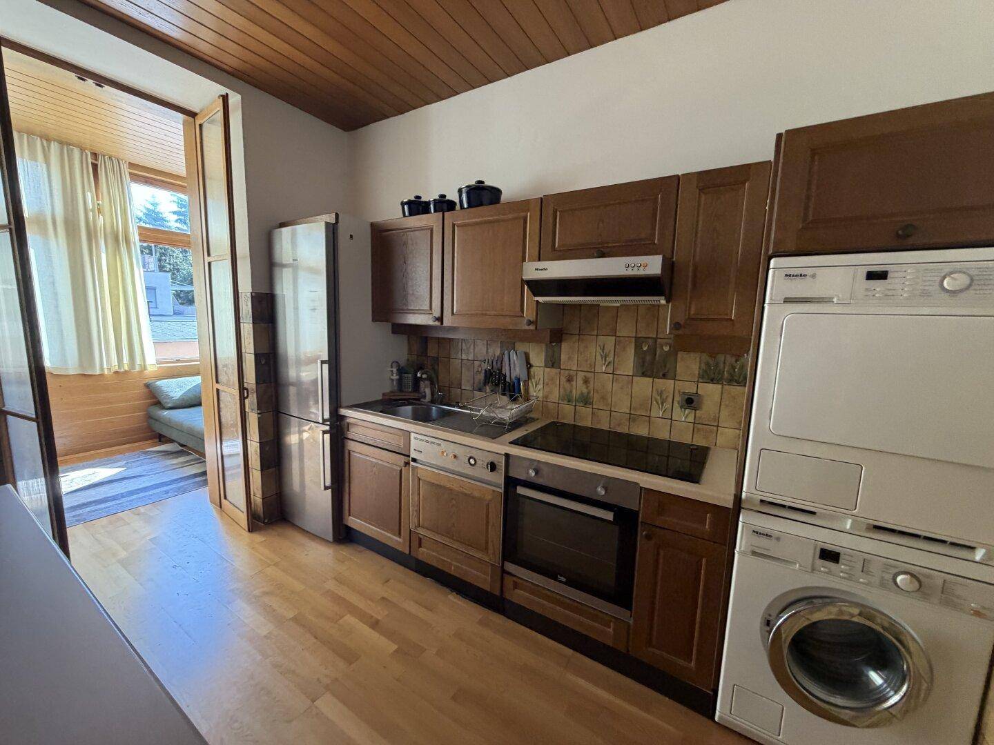 Funktionale Küche mit Holzschränken, integrierten Geräten und Zugang zum Wintergarten.