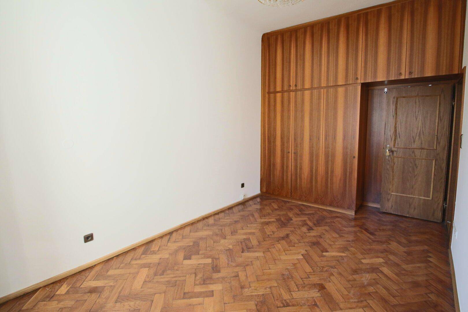 Geräumiges Zimmer mit Einbauschränken und klassischem Fischgrätparkett.