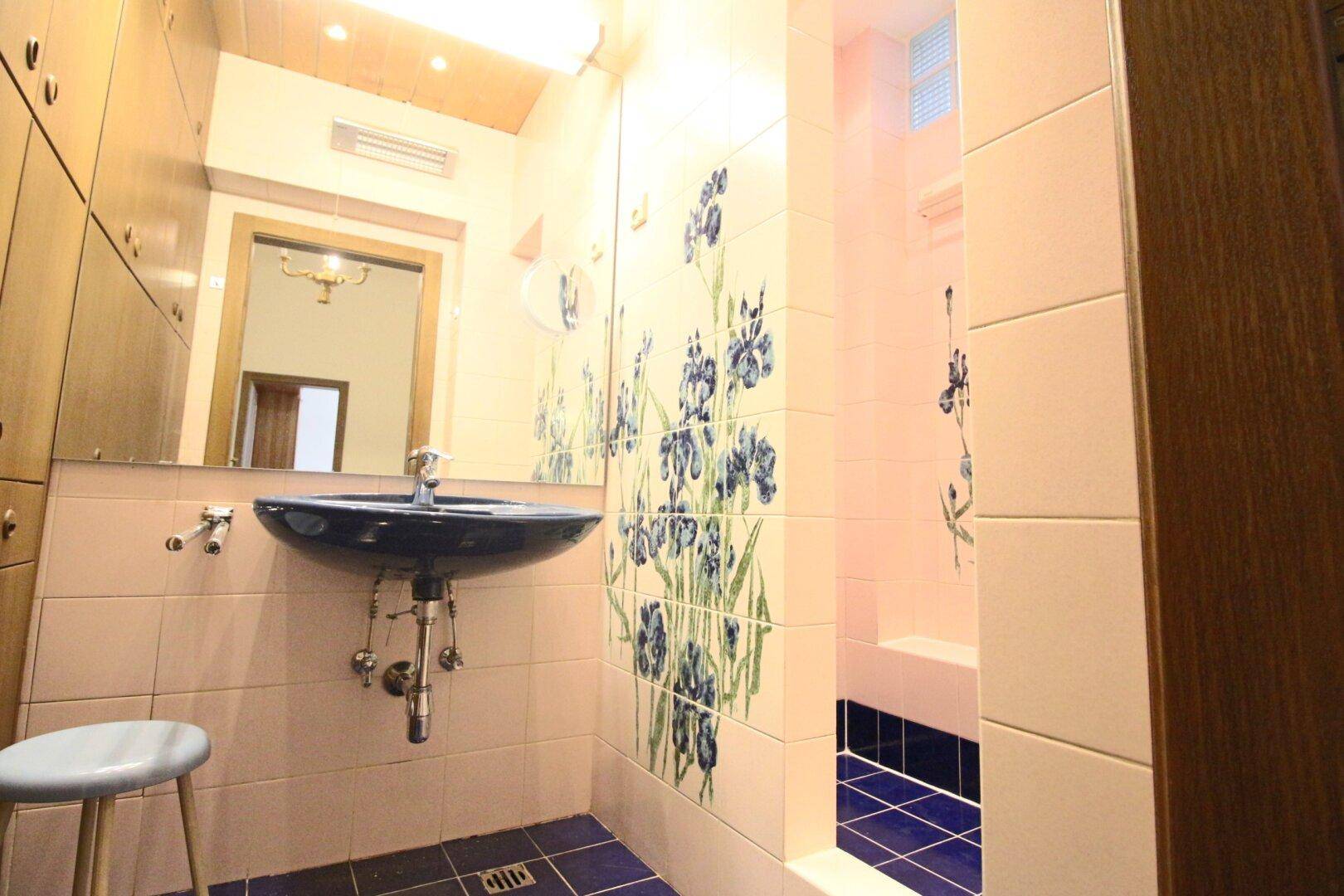 Badezimmer mit floralen Fliesen, Holzdecke und praktischem Spiegelschrank.