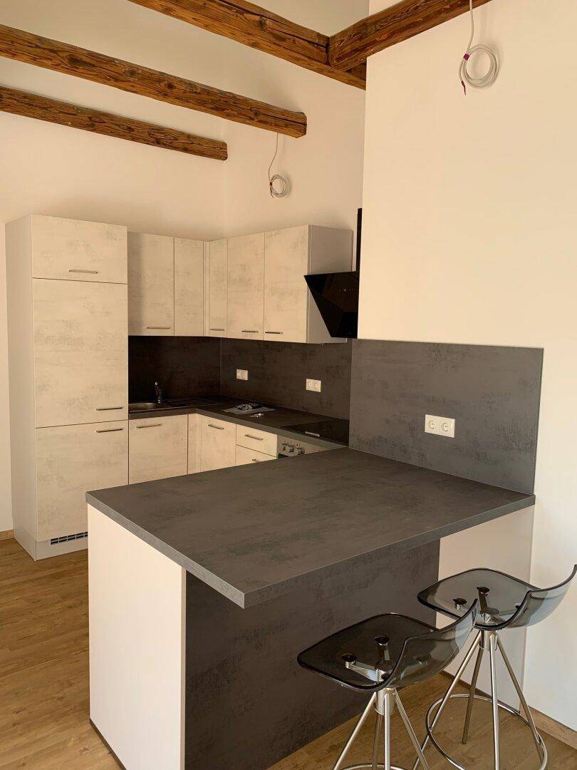 Neue Einbauküche mit Kücheninsel, modernen Geräten und sichtbaren Holzbalken an der Decke.
