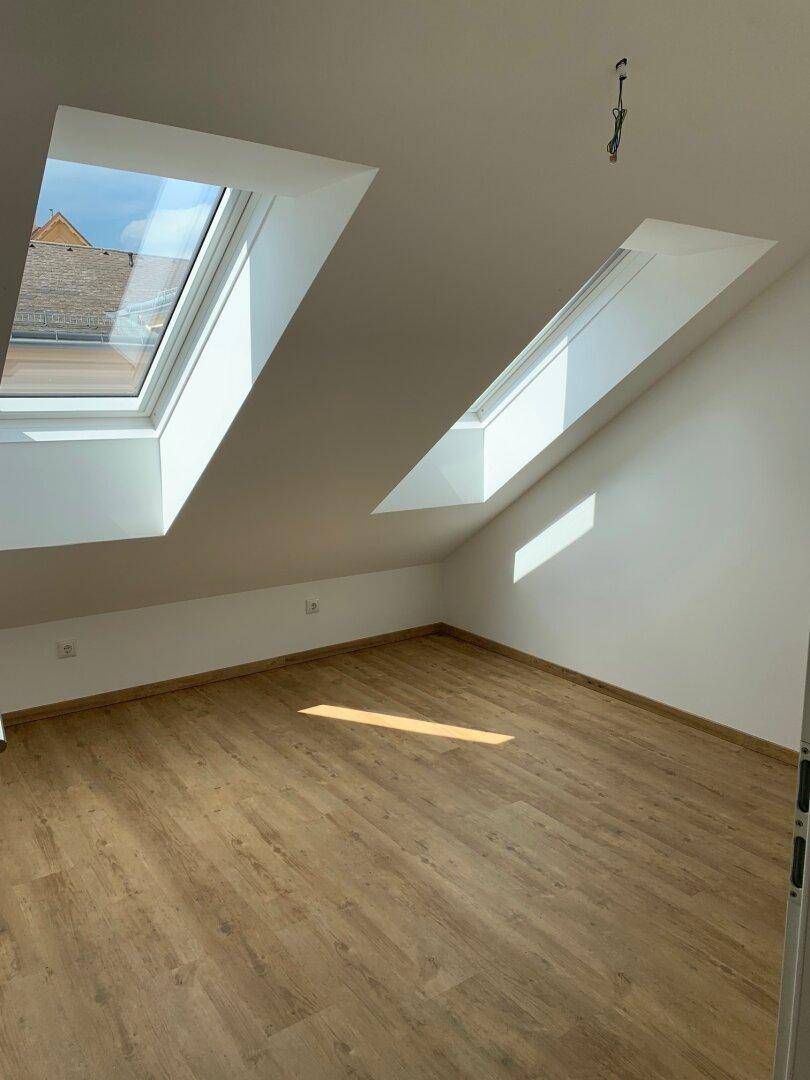 Helles Zimmer im Dachgeschoss mit Laminatboden und zwei großen Dachfenstern für viel Tageslicht.
