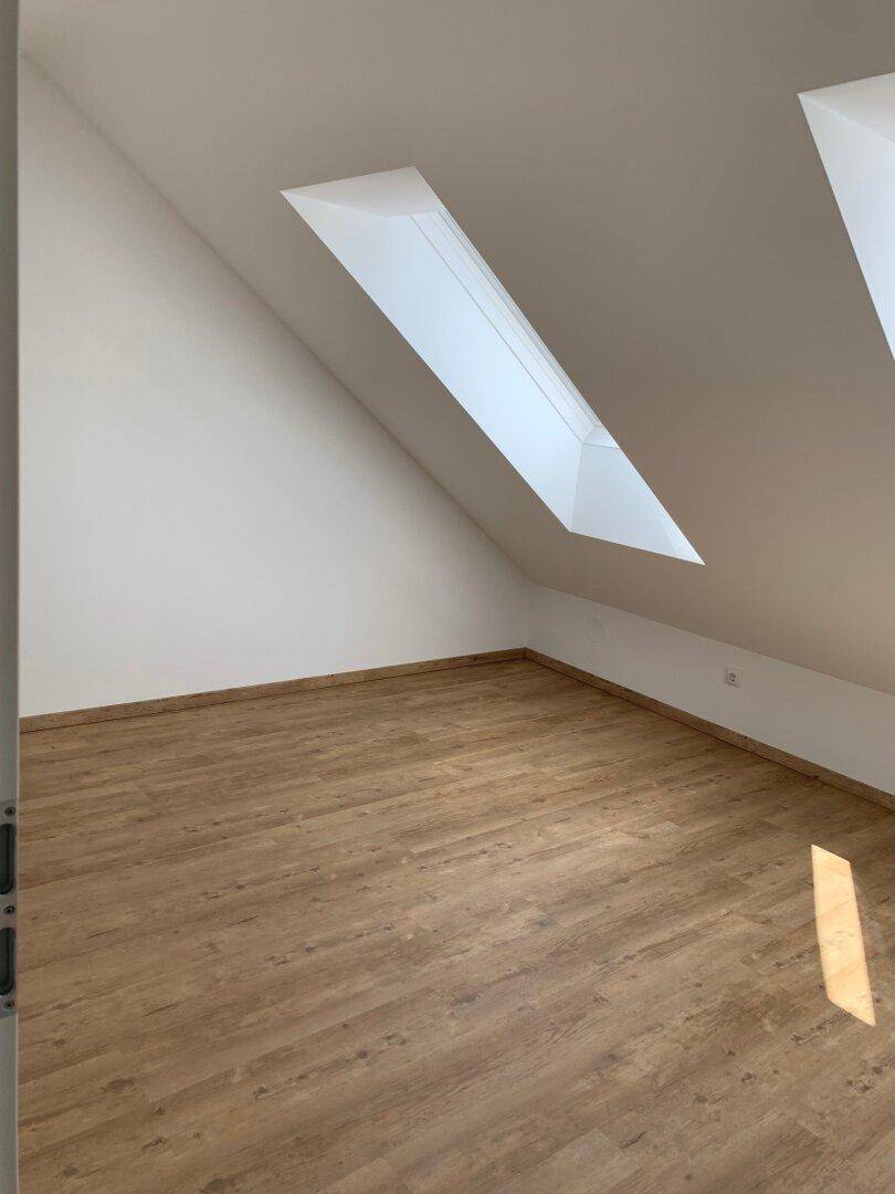 Geräumiges Zimmer im Dachgeschoss mit Laminatboden und einem großen Dachfenster, das viel Licht spendet.