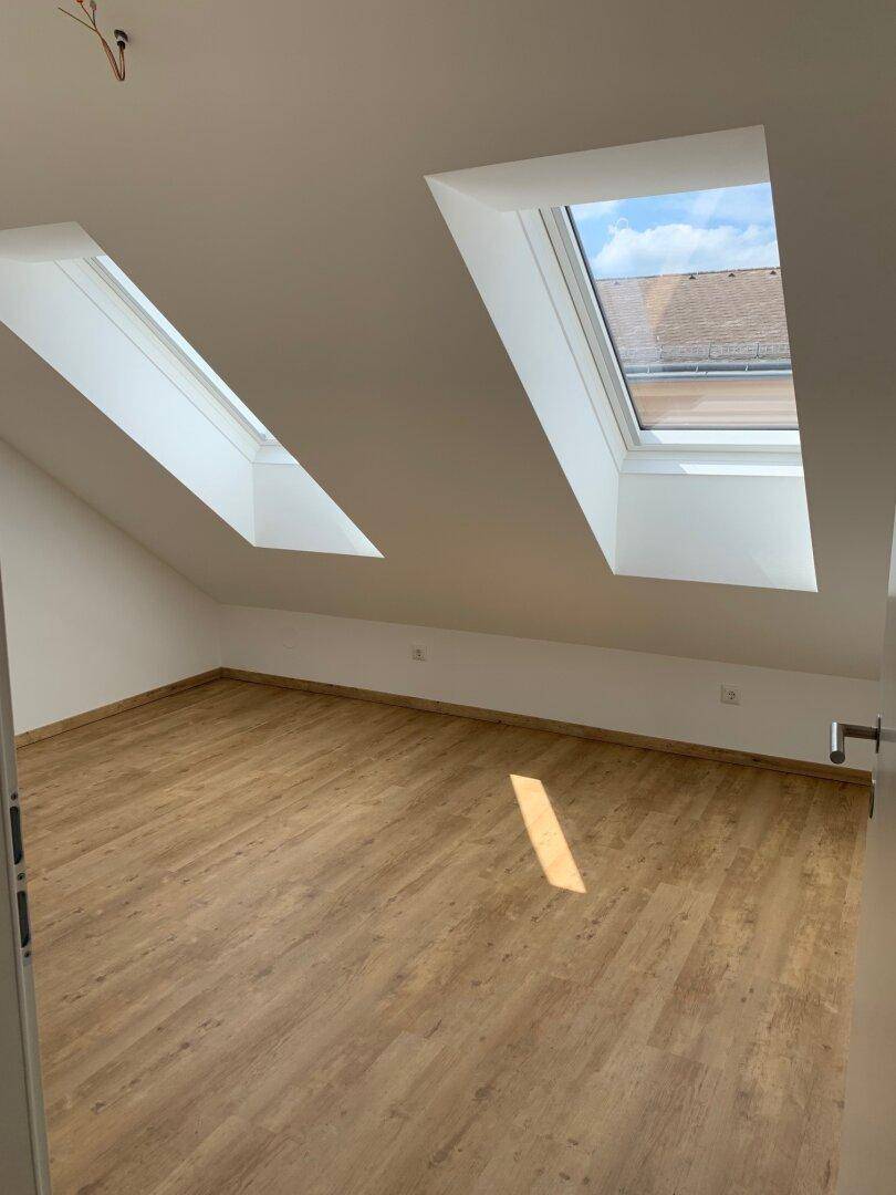Lichtdurchflutetes Dachzimmer mit Laminatboden und zwei schrägen Dachfenstern für eine helle Atmosphäre.