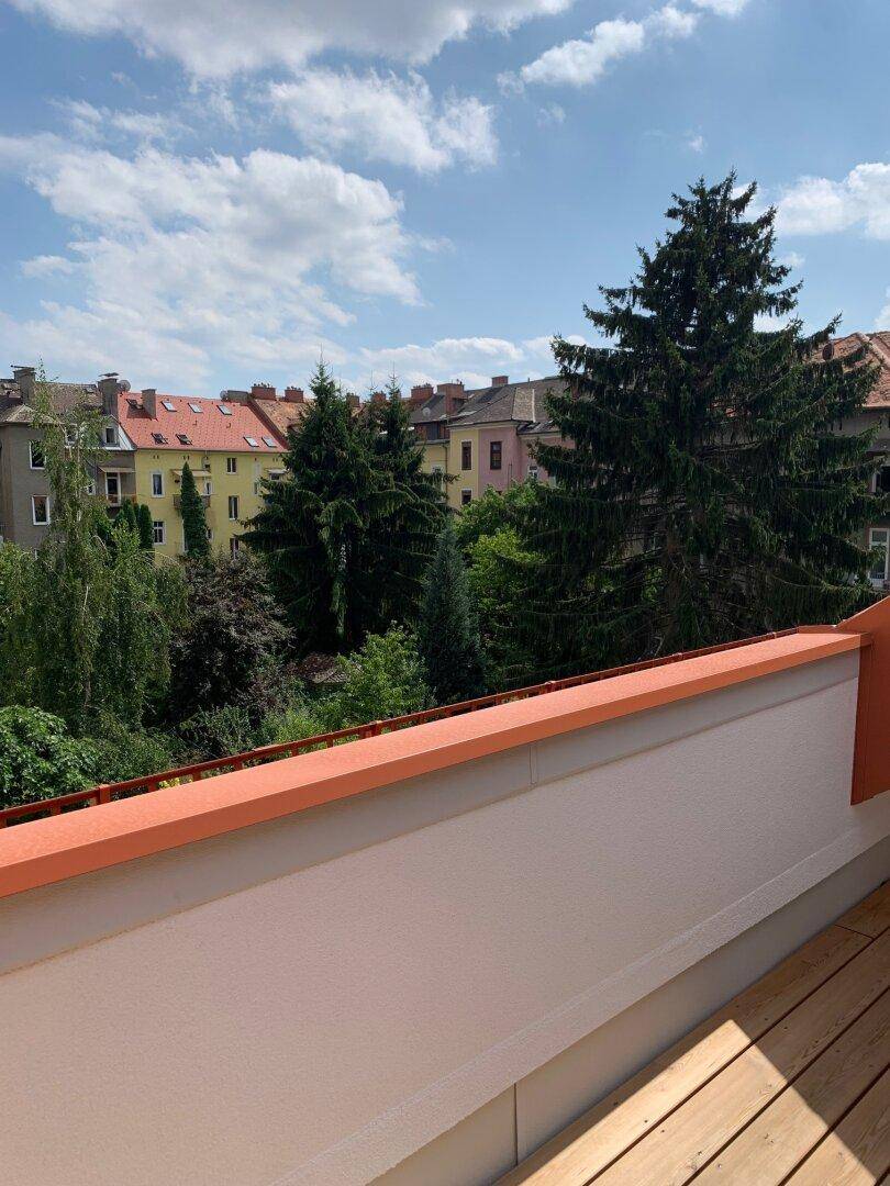 Sonniger Balkon mit Holzboden und weitem Blick über die Dächer und grüne Umgebung.