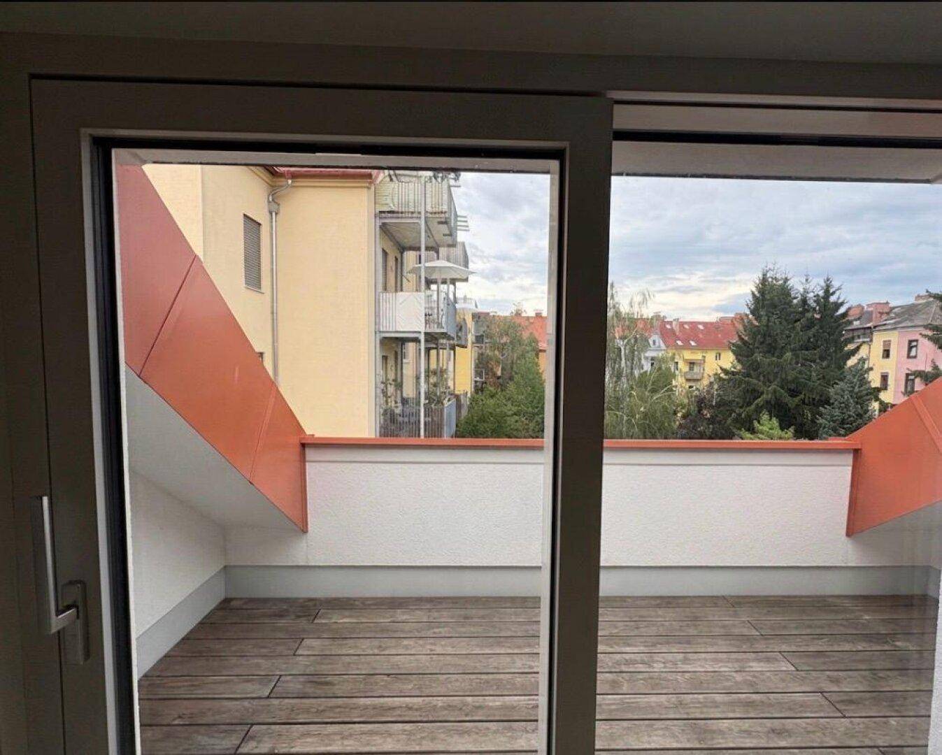 Geräumiger Balkon mit Holzboden und Blick auf die umliegenden Gebäude und Bäume.