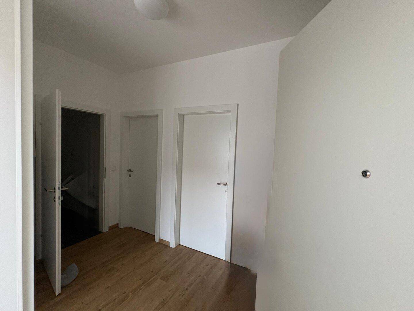 Heller Flur mit Laminatboden und mehreren weißen Türen, die zu den Zimmern führen.