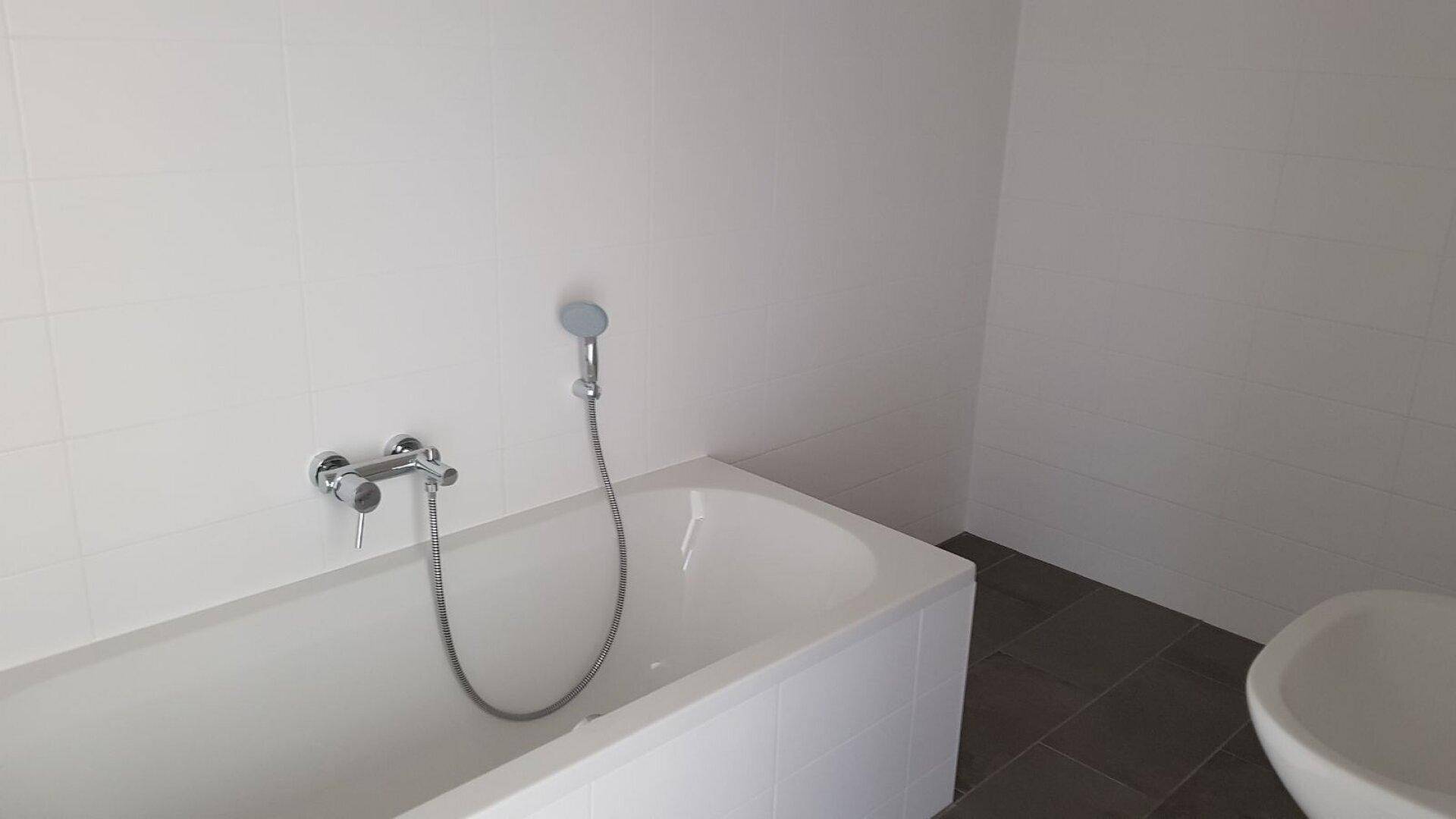 Modernes Badezimmer mit weißer Badewanne, hellen Wandfliesen und dunklem Fliesenboden.