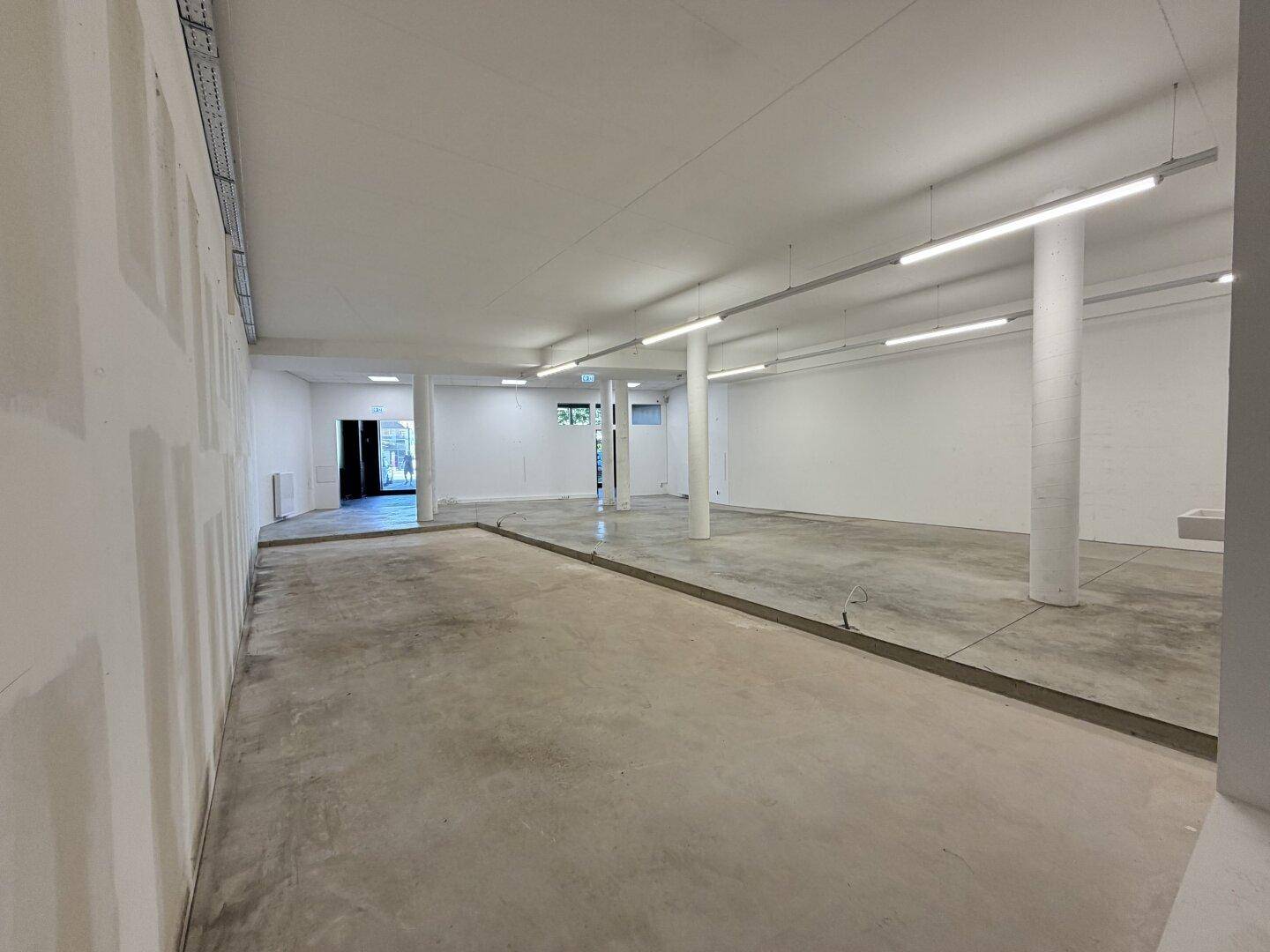 Geräumiger, heller Innenraum mit Betonboden und weißen Wänden, ausgestattet mit moderner Beleuchtung.