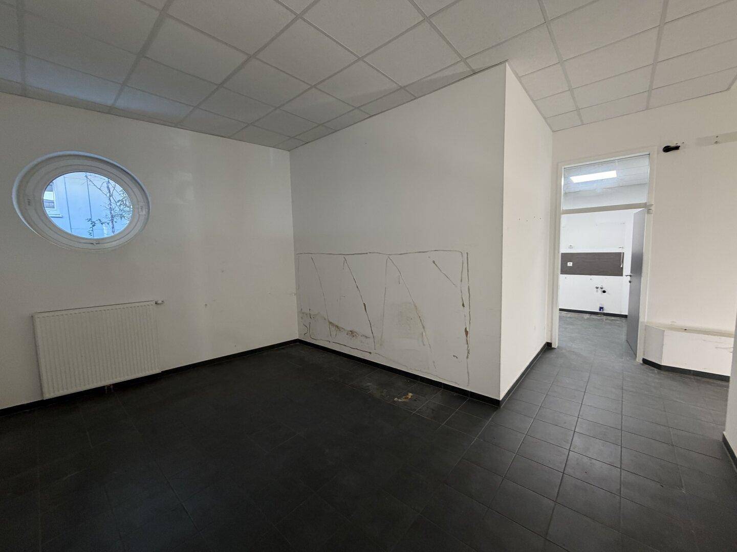 Kleiner Raum mit dunklem Fliesenboden, weiß gestrichenen Wänden und einem runden Fenster.