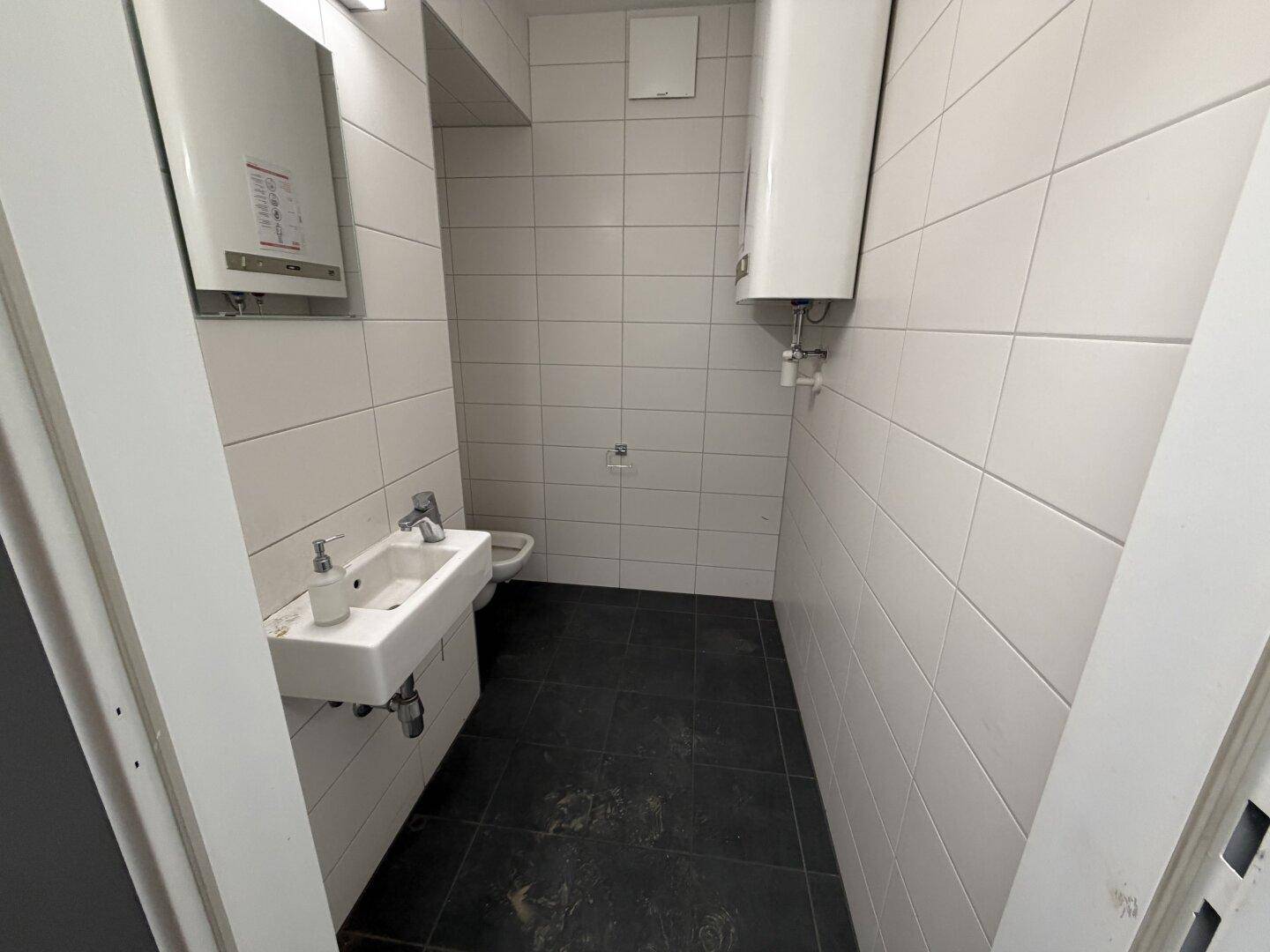 Kleiner WC-Raum mit weißen Fliesen, Waschbecken und Boiler, funktional und sauber.