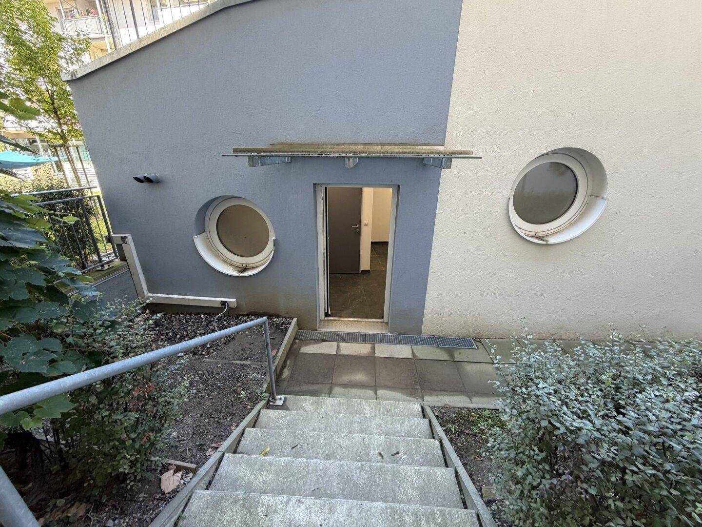 Außentreppe führt zu einem Eingang mit runden Fenstern und einer schlichten Überdachung.