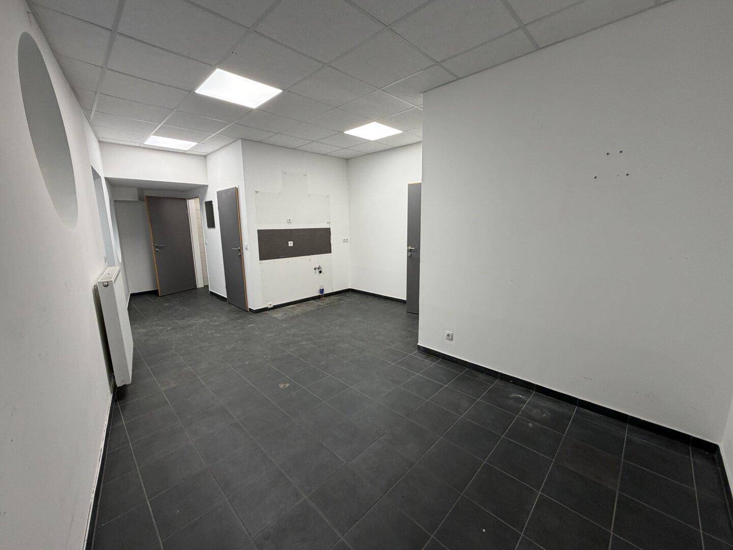 Heller Raum mit dunklem Fliesenboden und weißen Wänden, bietet mehrere Türen zu angrenzenden Bereichen.