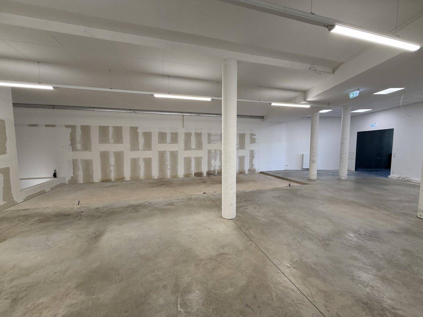 Großer, heller Raum mit Betonboden und weißen Wänden, ideal für gewerbliche Nutzung oder Lagerung.