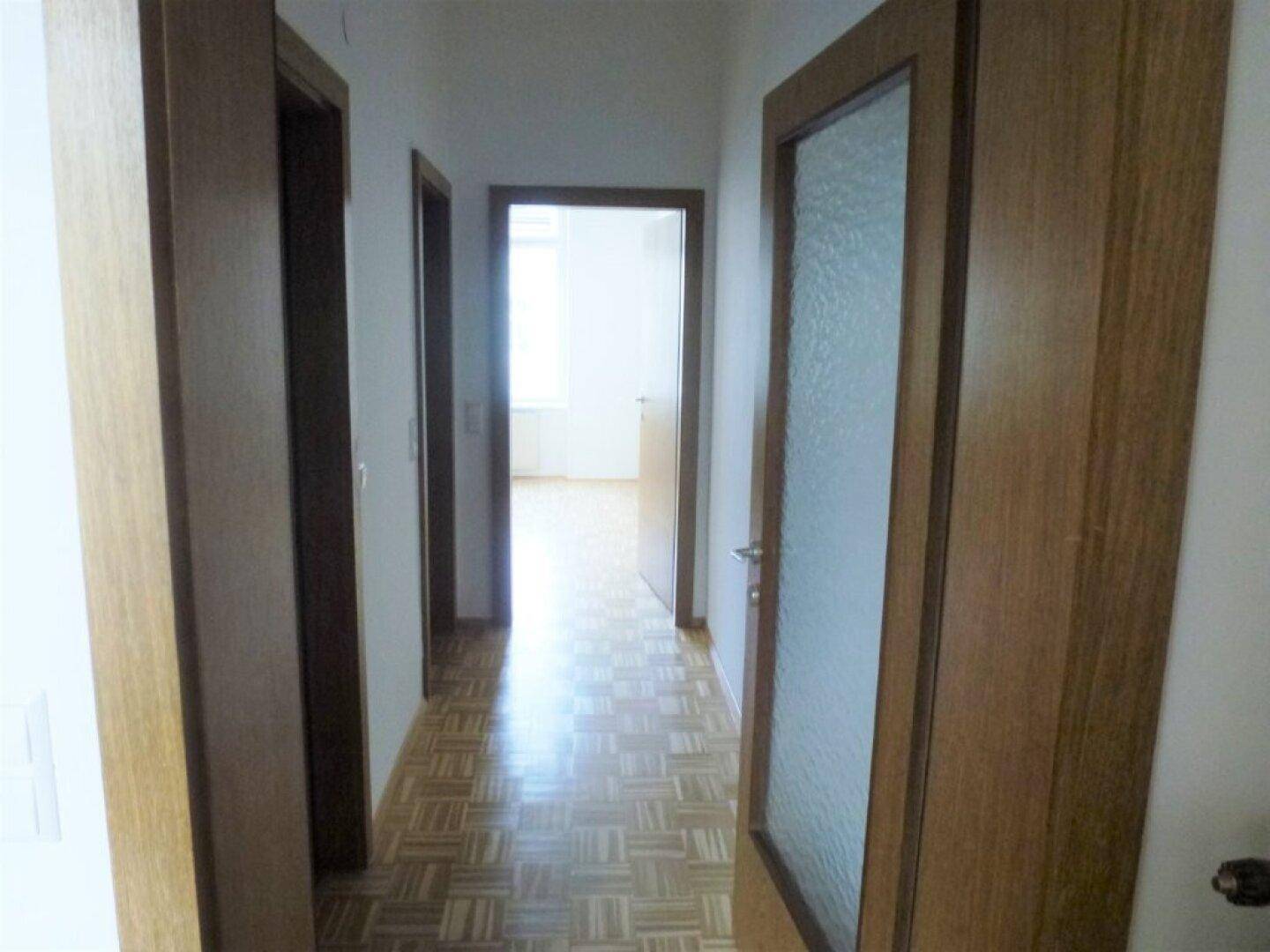 Heller Flur mit Holzparkettboden und mehreren Türen, darunter eine mit Milchglas.