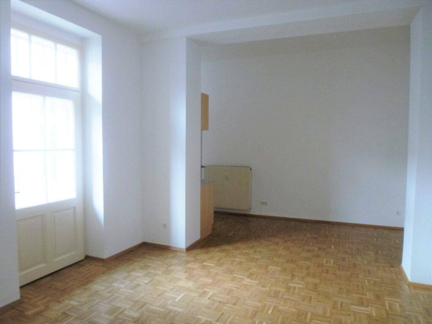 Geräumiges Wohnzimmer mit Holzparkettboden und Zugang zu einem Balkon oder einer Terrasse.
