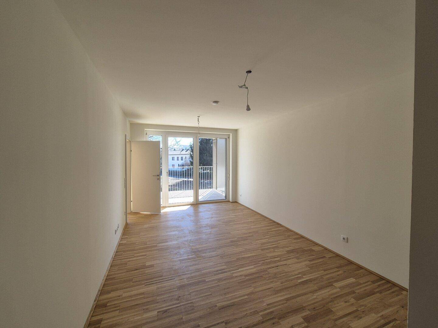 Helles, leeres Zimmer mit Parkettboden und Zugang zu einem Balkon, bereit zur individuellen Gestaltung.