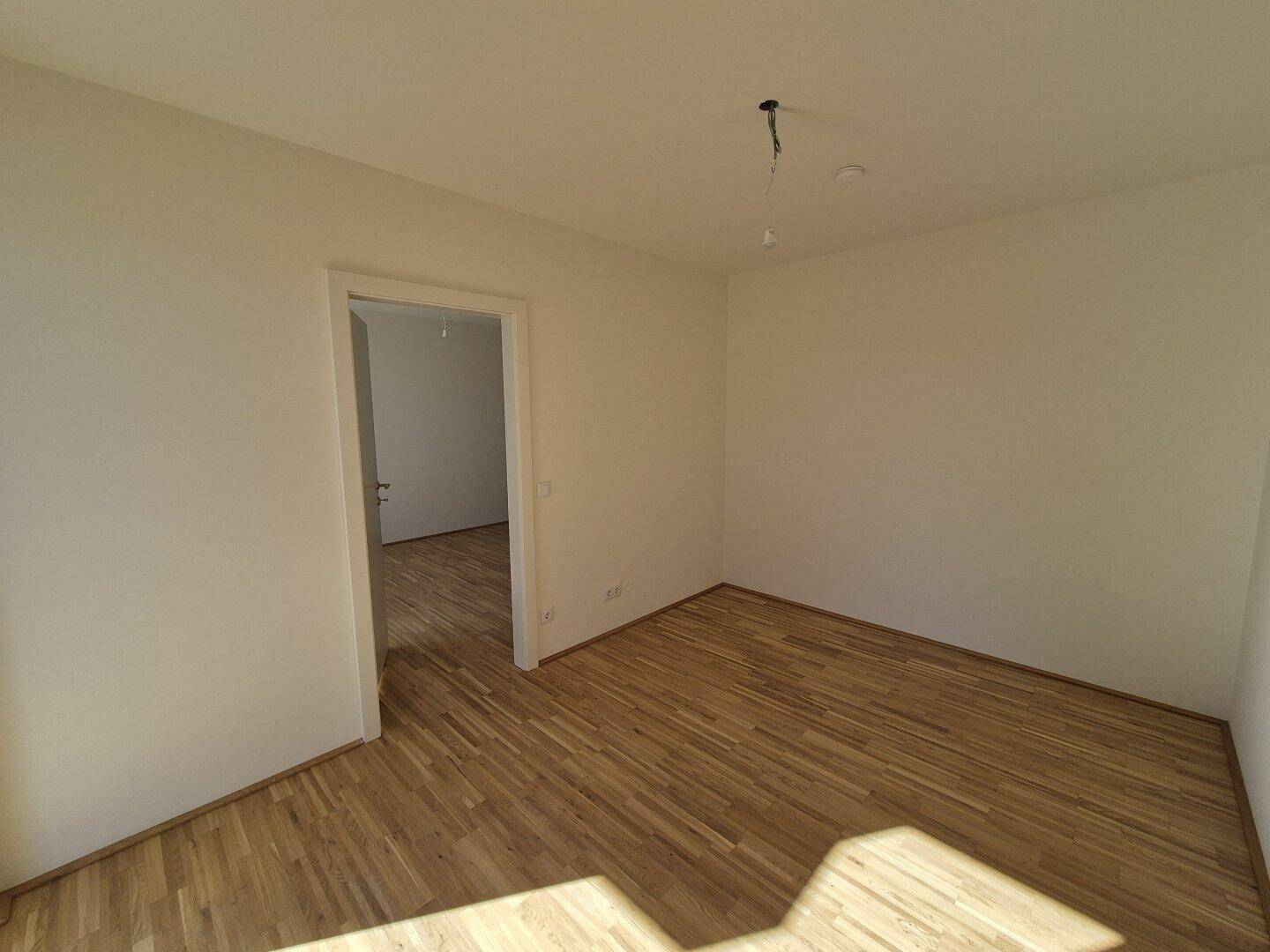 Leeres Zimmer mit hellem Parkettboden und weiß gestrichenen Wänden, bereit für neue Bewohner.