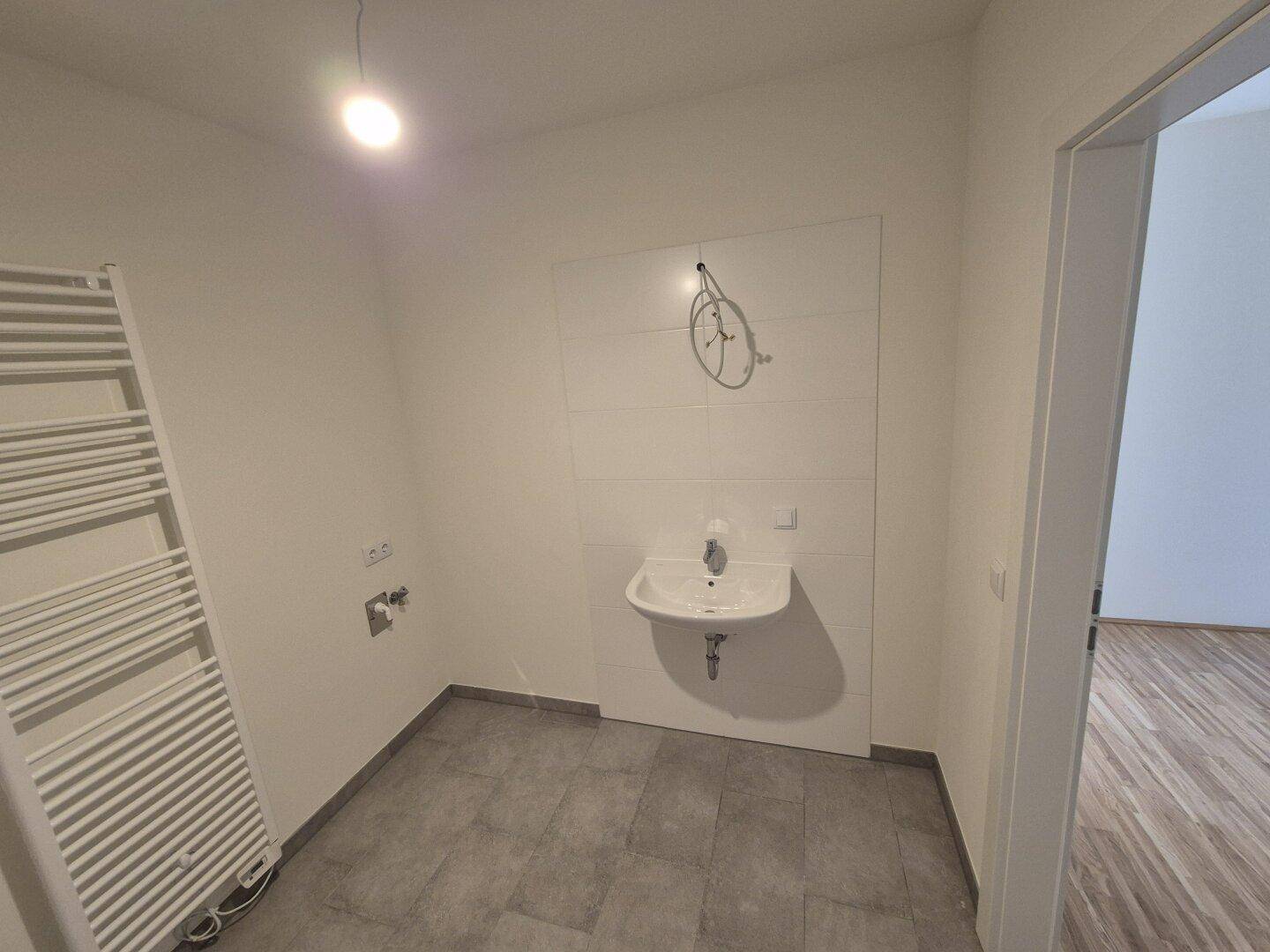 Modernes Badezimmer mit Einzelwaschbecken, grauen Fliesen und einem beheizten Handtuchhalter.