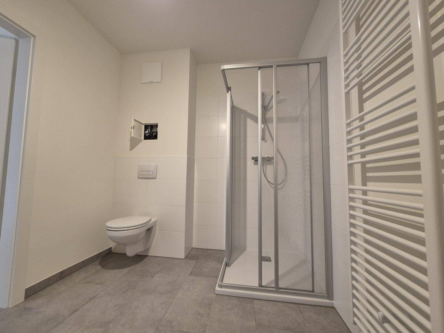 Helles Badezimmer mit Duschkabine, wandhängendem WC und beheiztem Handtuchhalter.