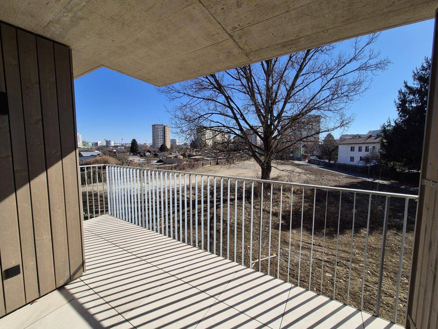 Balkon mit weitem Blick auf eine Grünfläche und entfernte Gebäude unter klarem Himmel.