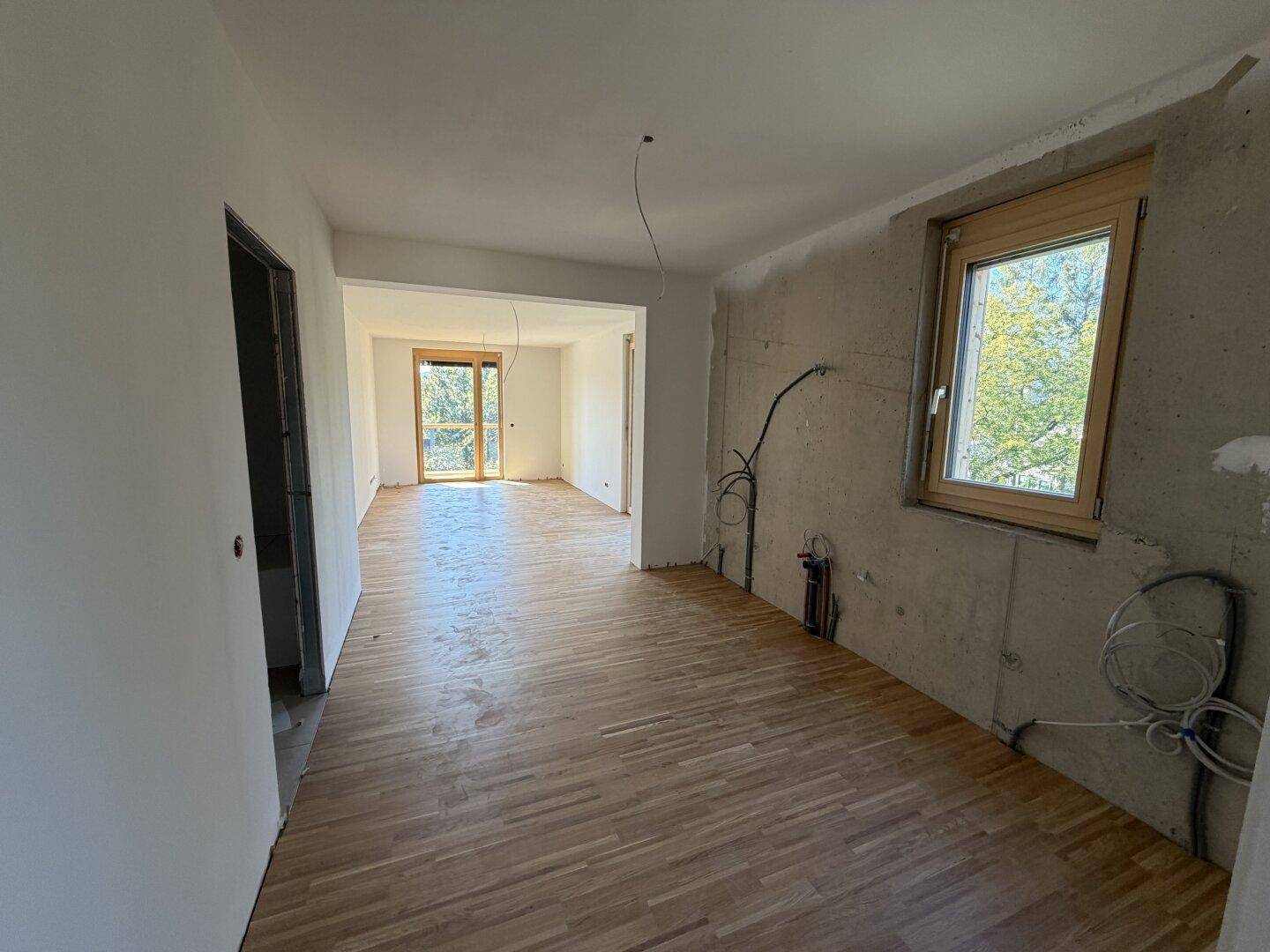 Geräumiger Wohnbereich im Rohbau mit Parkettboden und Blick ins Grüne, bereit für den Ausbau.