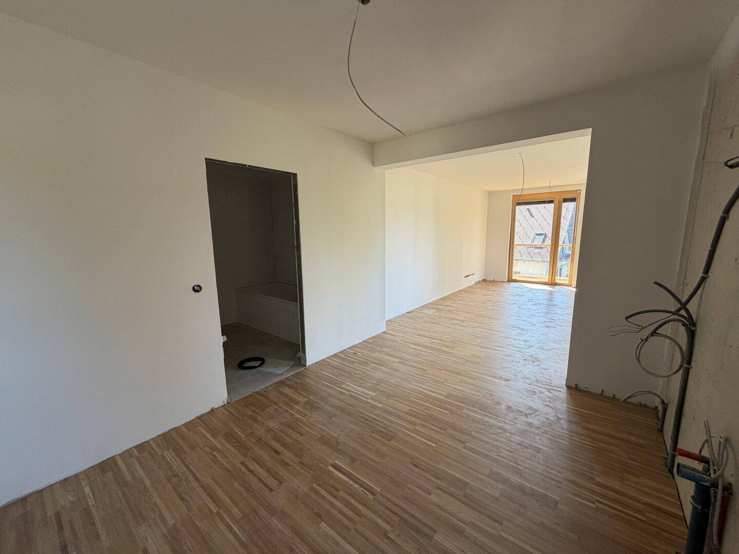 Offener Wohnbereich im Rohbau mit Parkettboden und Durchgang zu weiteren Zimmern, viel Potenzial.