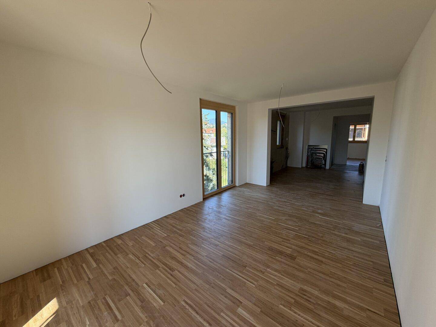 Geräumiger Wohnbereich im Rohbau mit Parkettboden und Zugang zum französischen Balkon.