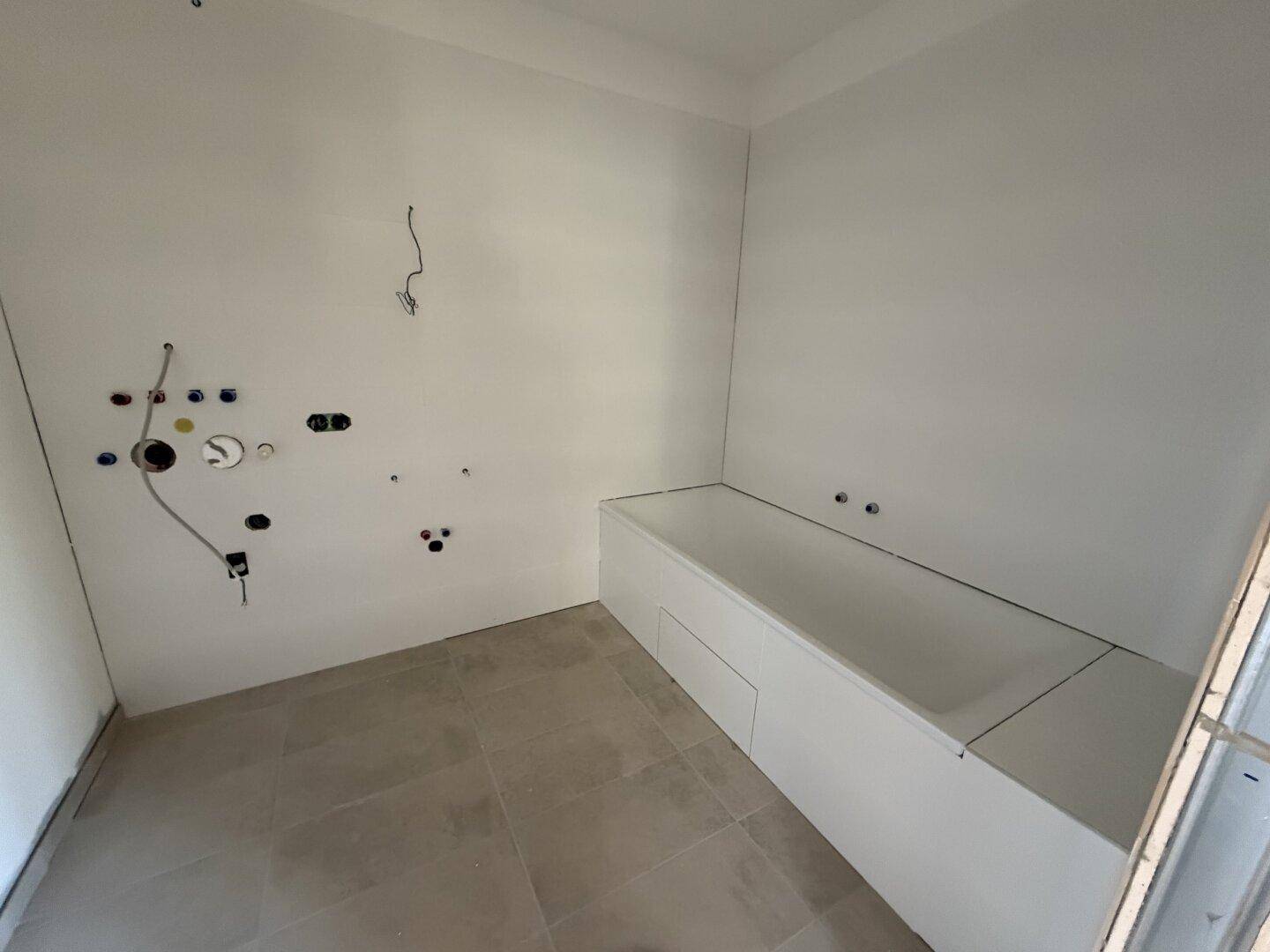 Badezimmer im Rohbau mit bereits installierter Badewanne und Fliesenboden, bereit für die Fertigstellung.
