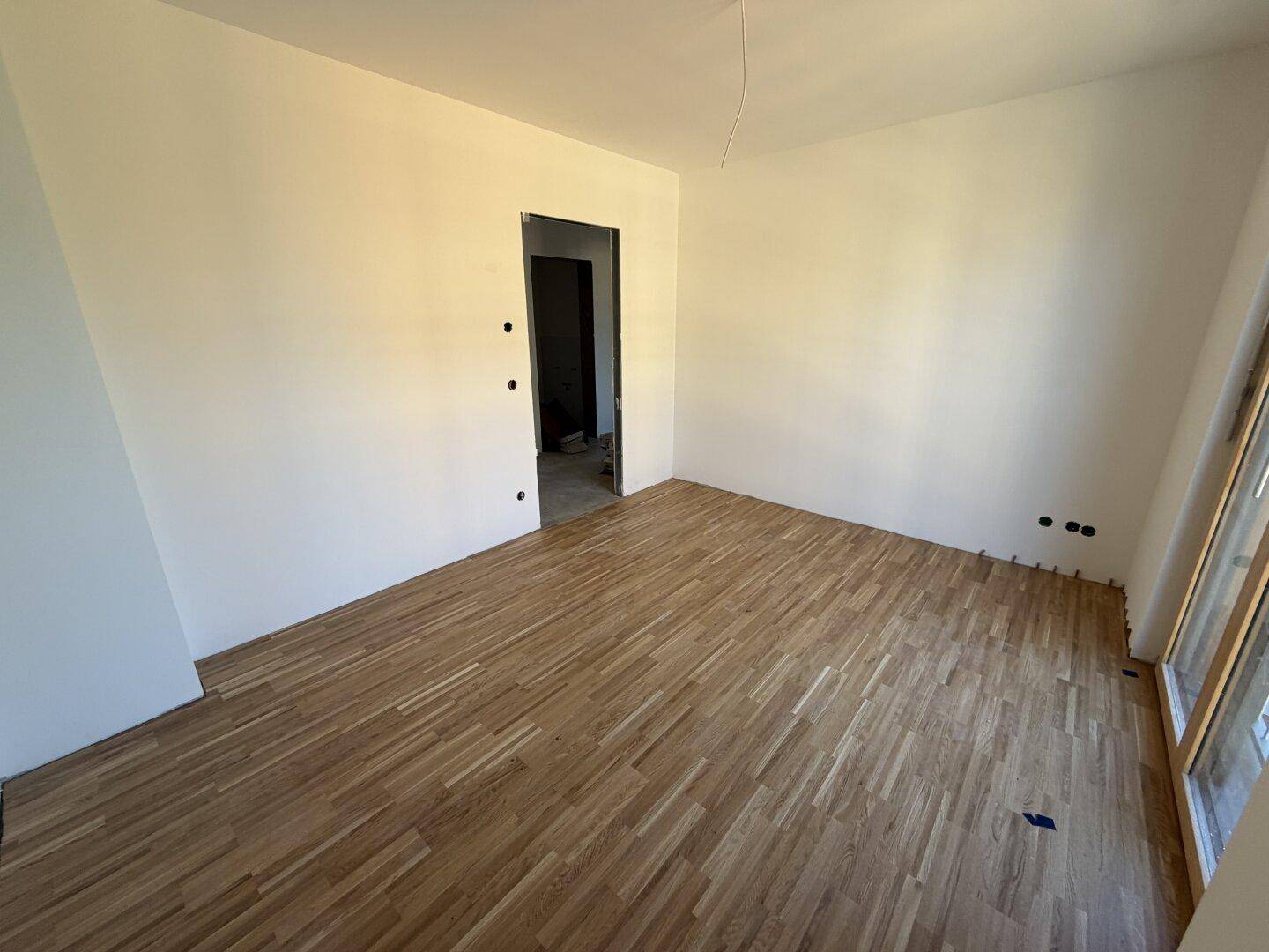 Helles Zimmer mit Parkettboden und Türöffnung zu einem weiteren Raum, vielseitig nutzbar.