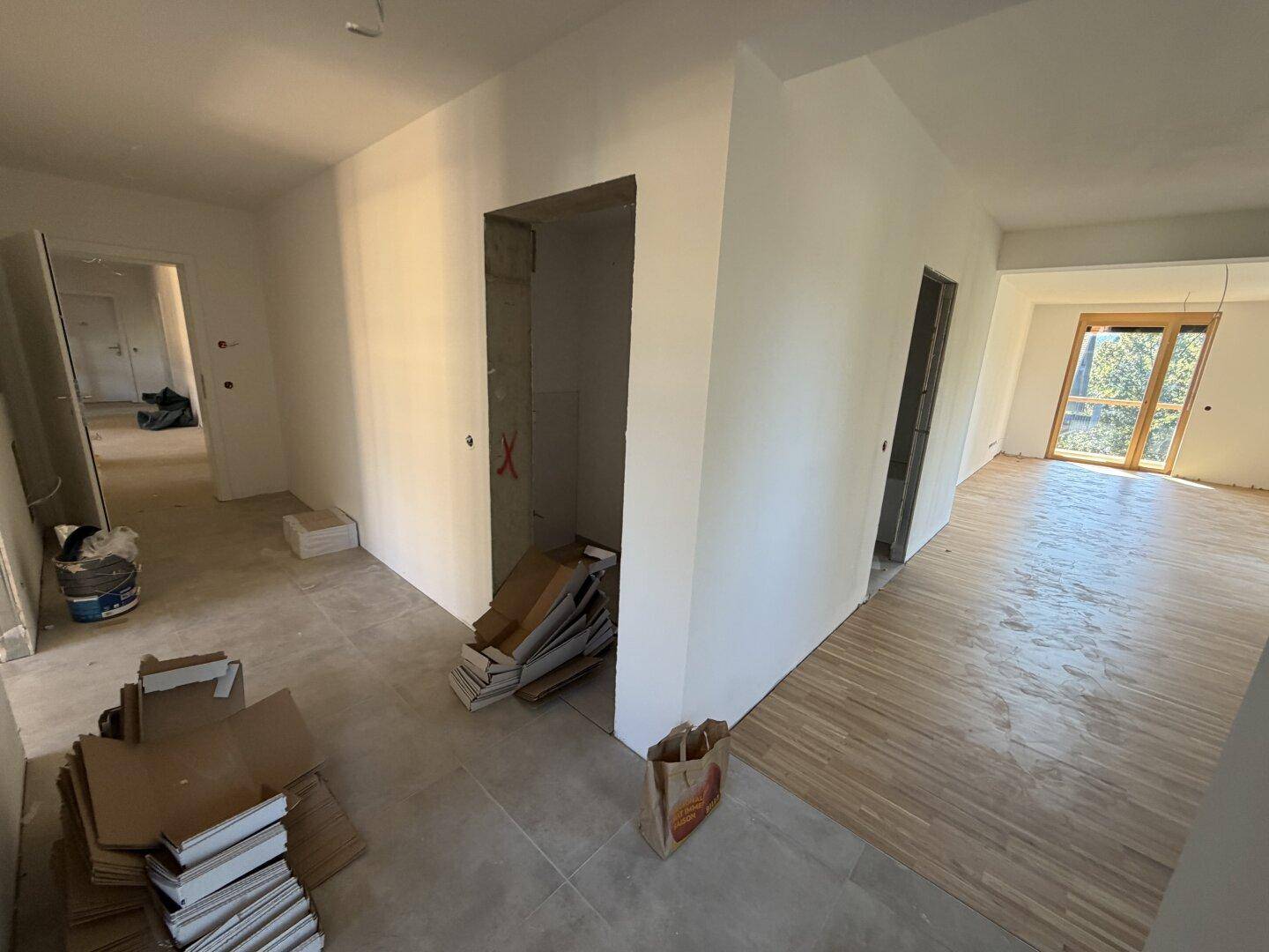 Eingangsbereich im Rohbau mit Fliesen- und Parkettboden und Zugang zu verschiedenen Räumen.