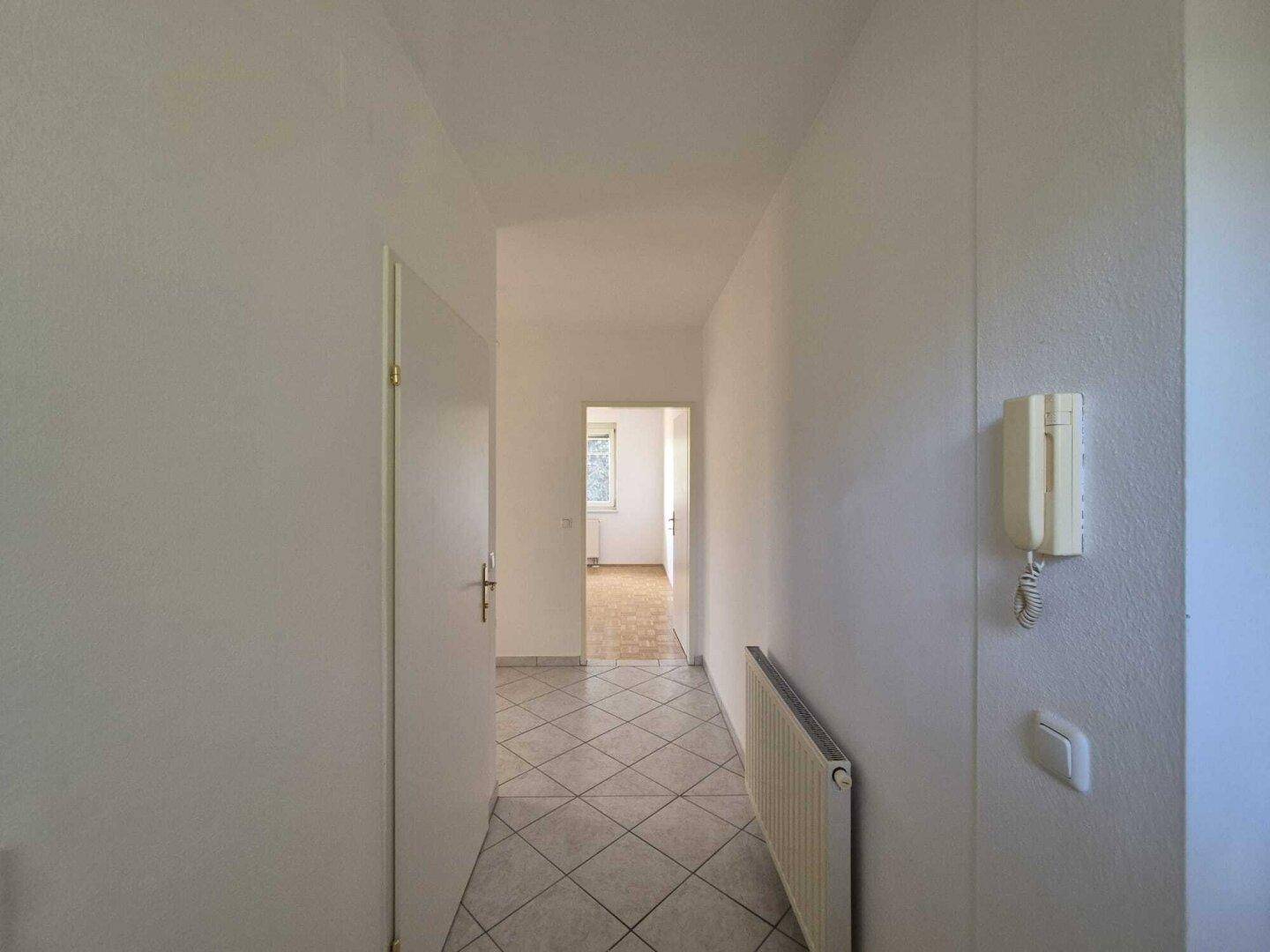 Heller Flur mit Fliesenboden und Gegensprechanlage, der zu den verschiedenen Zimmern führt.