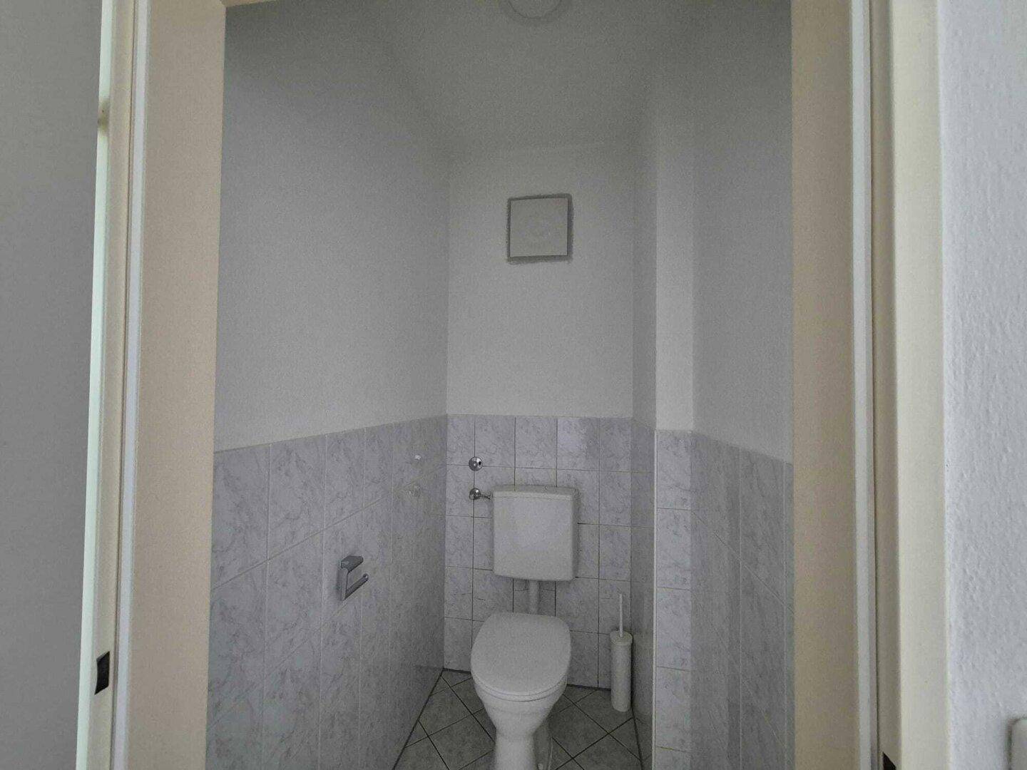 Separates WC mit Wandfliesen und einfacher Toilette, praktisch für Gäste.