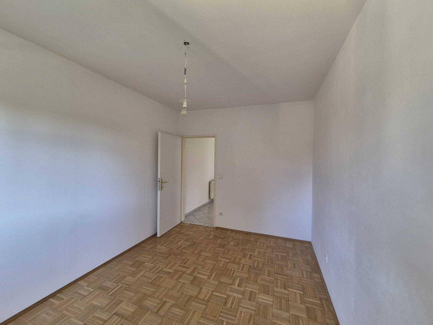 Ruhiges, leeres Zimmer mit Parkettboden und weiß gestrichenen Wänden, bereit zur Einrichtung.