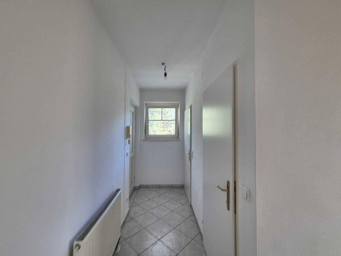 Langer Flur mit Fliesenboden und Fenster am Ende, das für natürliches Licht sorgt.