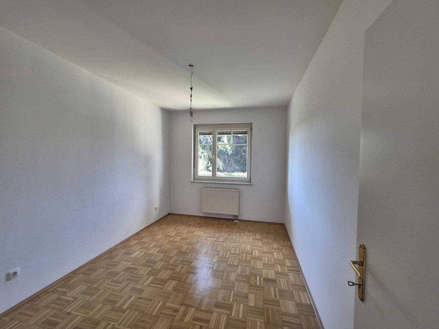 Helles Schlafzimmer mit Parkettboden und Fenster mit Blick ins Grüne, ideal für erholsame Nächte.
