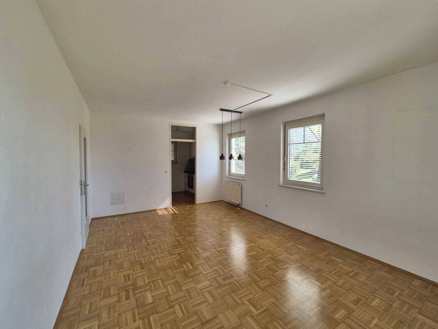 Helles, leeres Zimmer mit Fischgrätparkett und zwei Fenstern, bereit zur individuellen Gestaltung.
