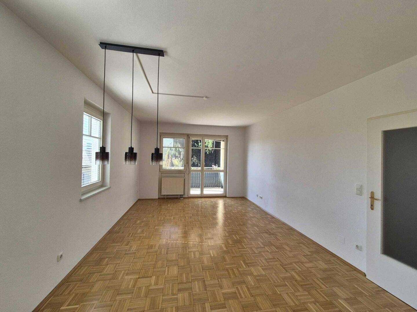Geräumiges Wohnzimmer mit Parkettboden und direktem Zugang zu einem sonnigen Balkon.