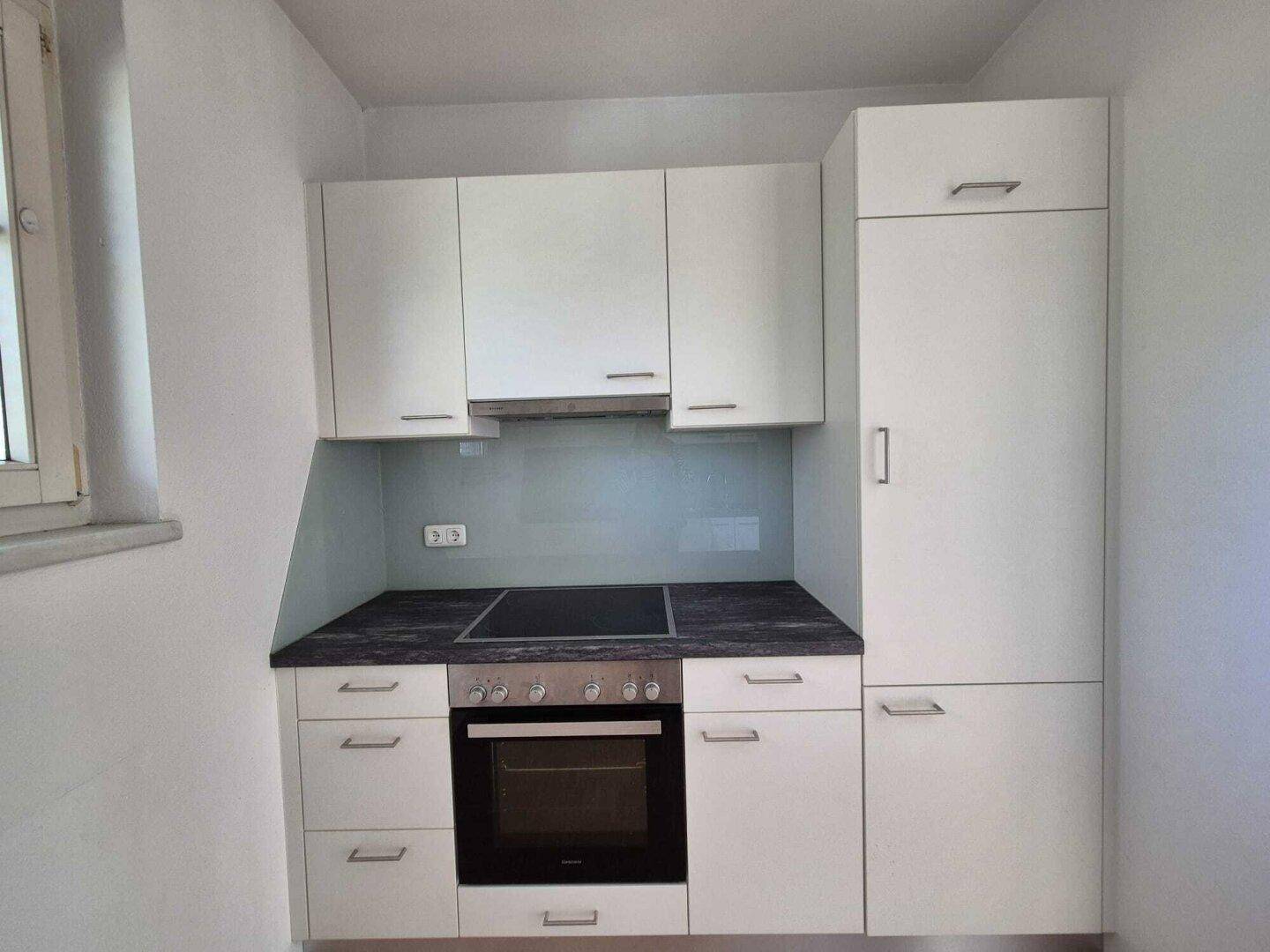 Kompakte Küchenzeile mit integriertem Backofen, Induktionskochfeld und Stauraum für einen Kühlschrank.