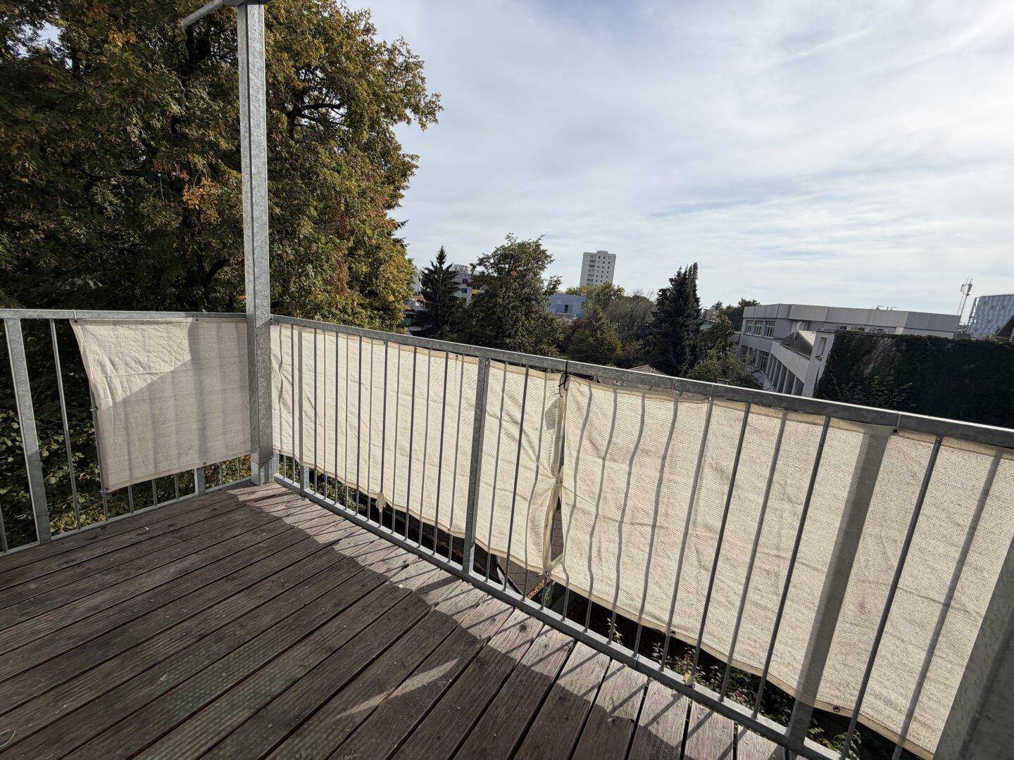 Balkon mit Holzboden und Metallgeländer, umgeben von Bäumen und Blick auf die Umgebung.