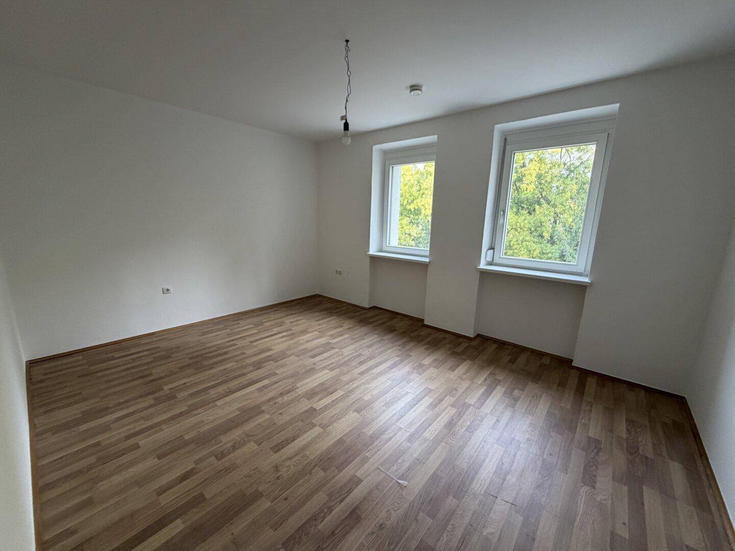 Geräumiges Schlafzimmer mit Laminatboden und Fenstern, die viel Tageslicht und Grünblick bieten.