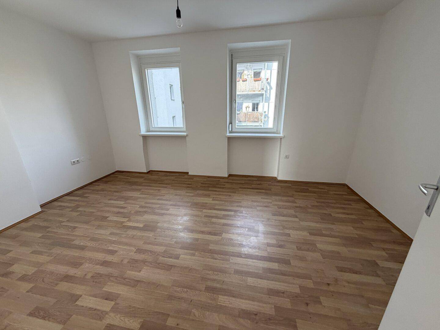 Schlafzimmer mit Laminatboden und Fenstern, die einen Blick auf die umliegenden Gebäude ermöglichen.