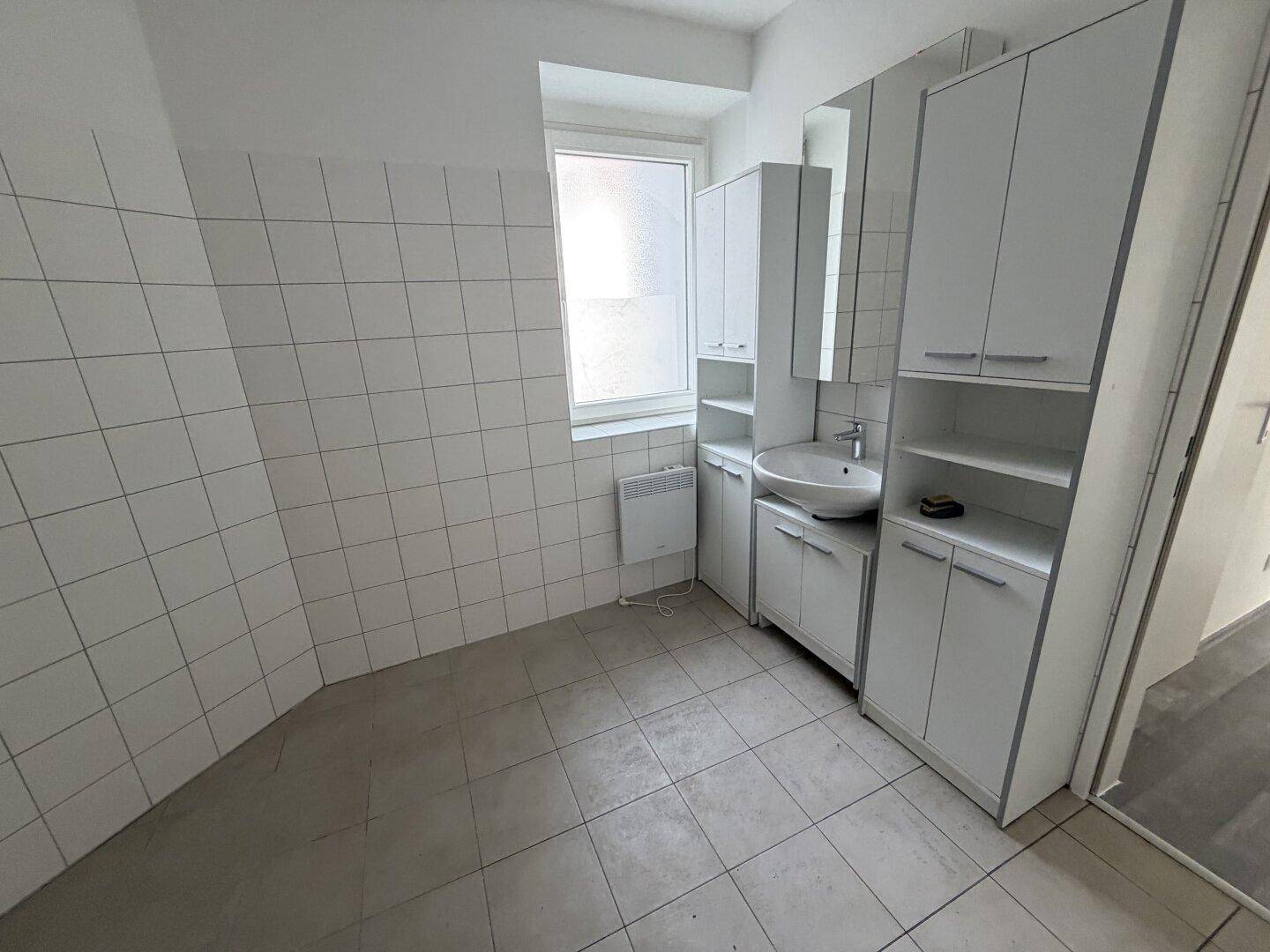 Badezimmer mit Waschbecken, Spiegelschrank, weißen Fliesen und einem Fenster für Tageslicht.