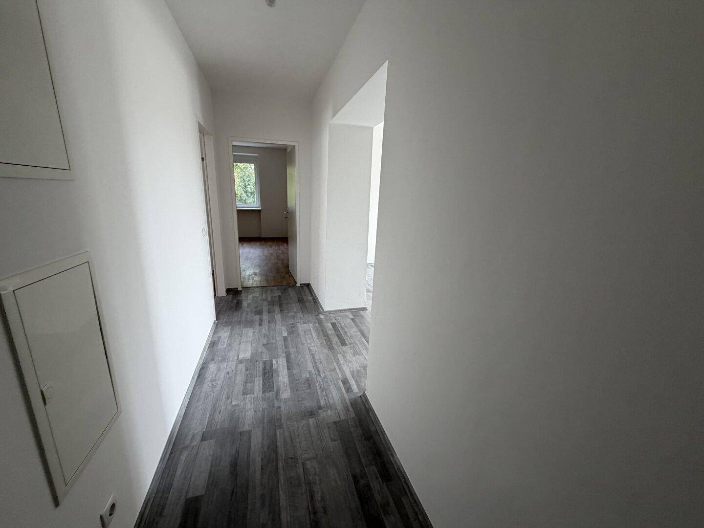 Heller Flur mit grauem Laminatboden und weißen Wänden, der zu verschiedenen Zimmern führt.