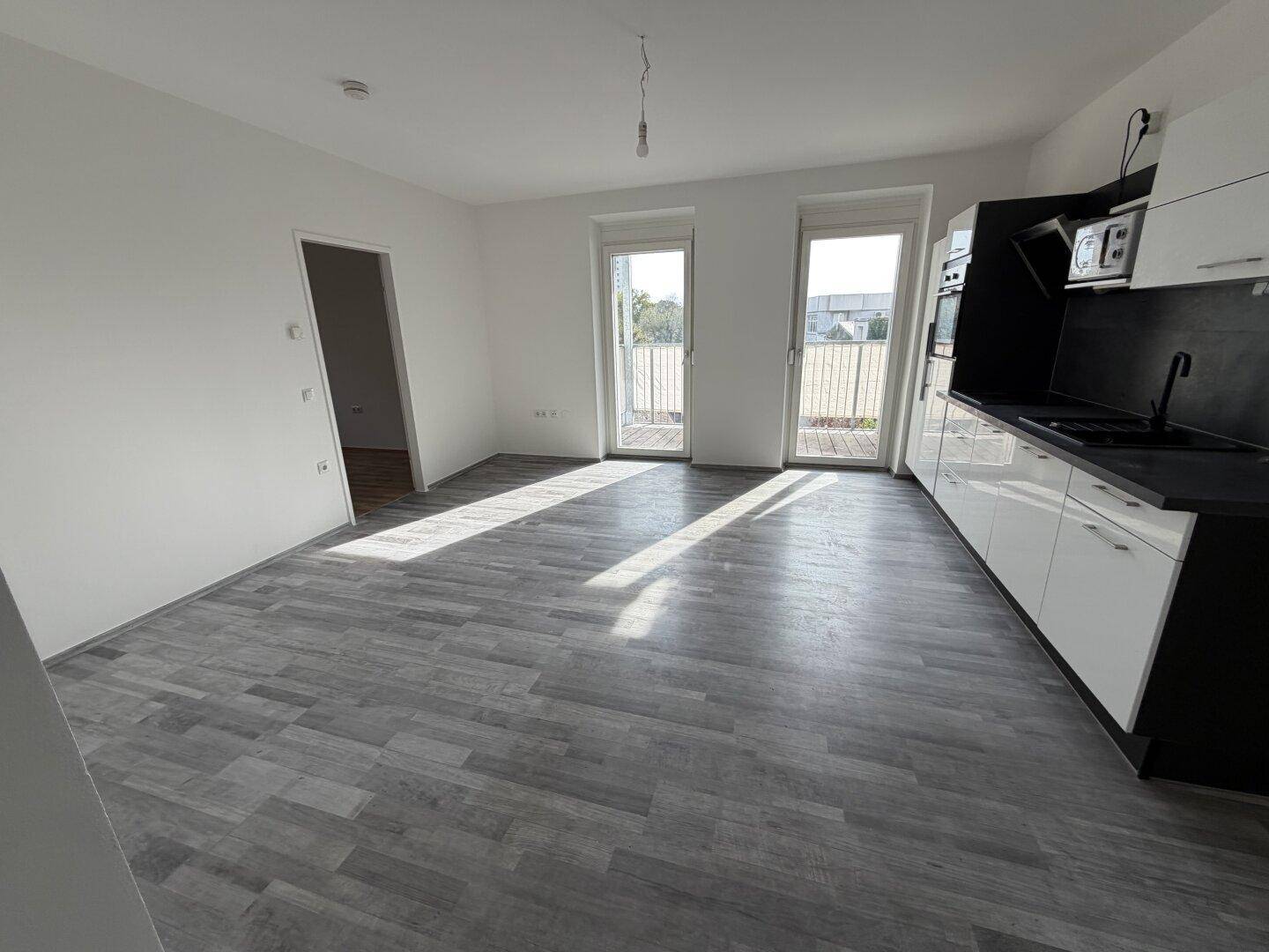 Lichtdurchfluteter Wohn- und Küchenbereich mit modernem Design, grauem Laminat und Balkonzugang.