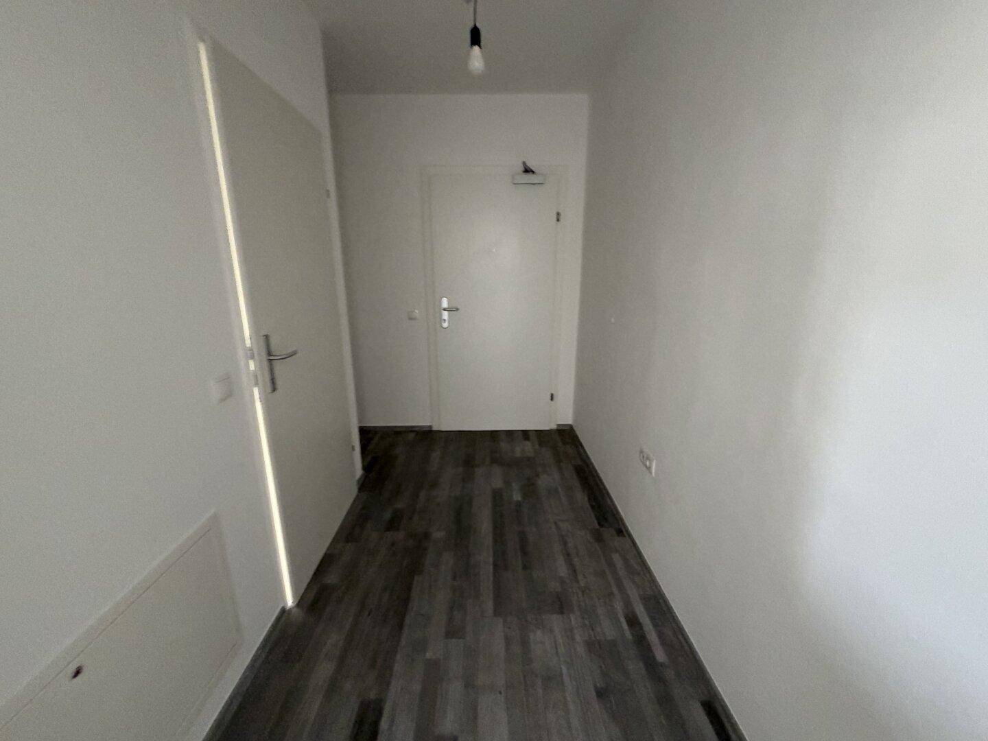 Eingangsbereich mit grauem Laminatboden und weißen Wänden, der zu den Wohnräumen führt.