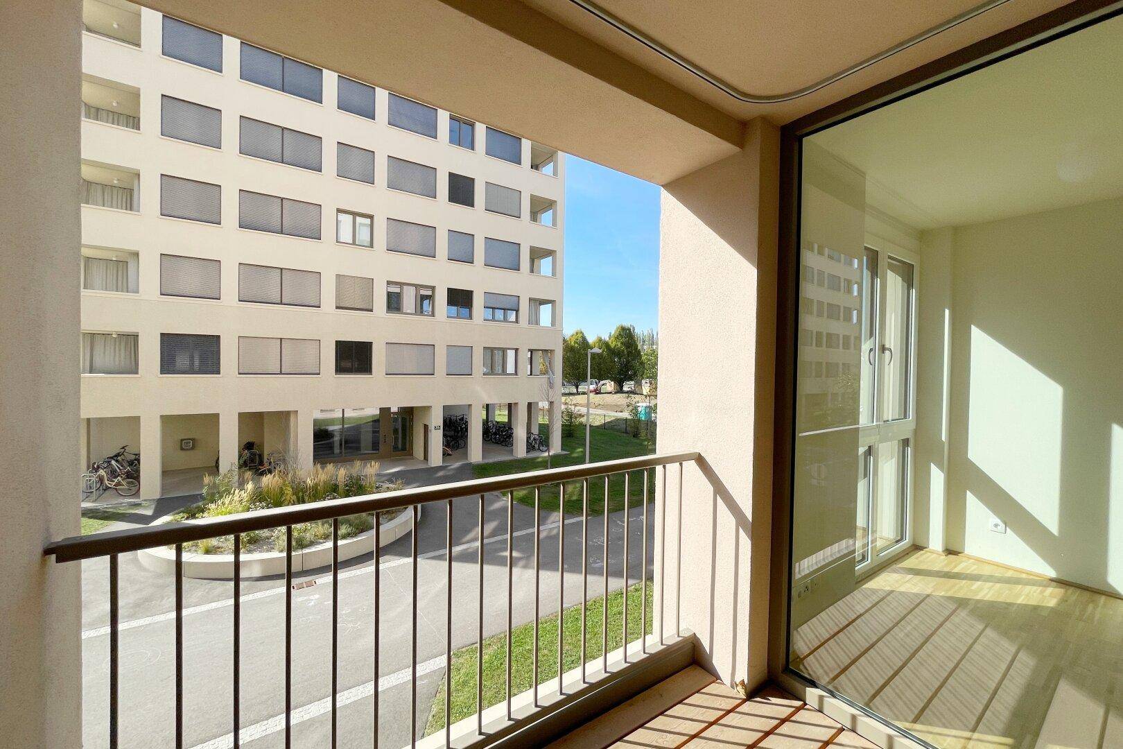 Sonnenverwöhnter Balkon mit Blick auf den gepflegten Innenhof und die moderne Architektur des Gebäudes.