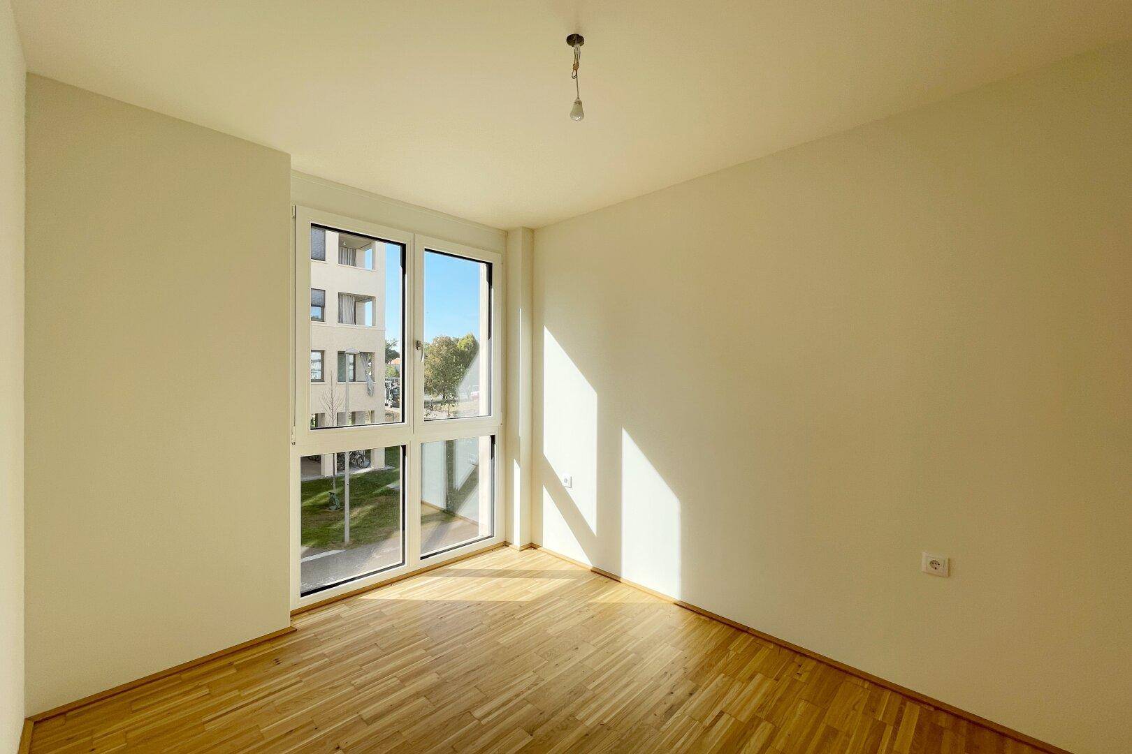 Helles Schlafzimmer oder Arbeitszimmer mit Holzboden und großen Fenstern, die viel Licht hereinlassen.